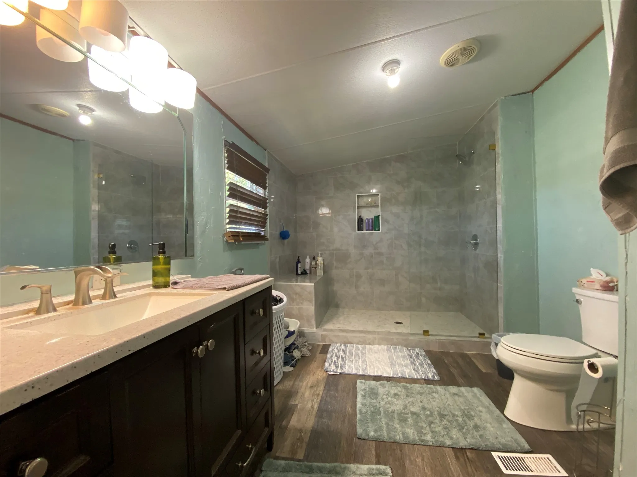 Bathroom featuring vanity, walk in shower, dark wood-style floors, and vaulted ceiling