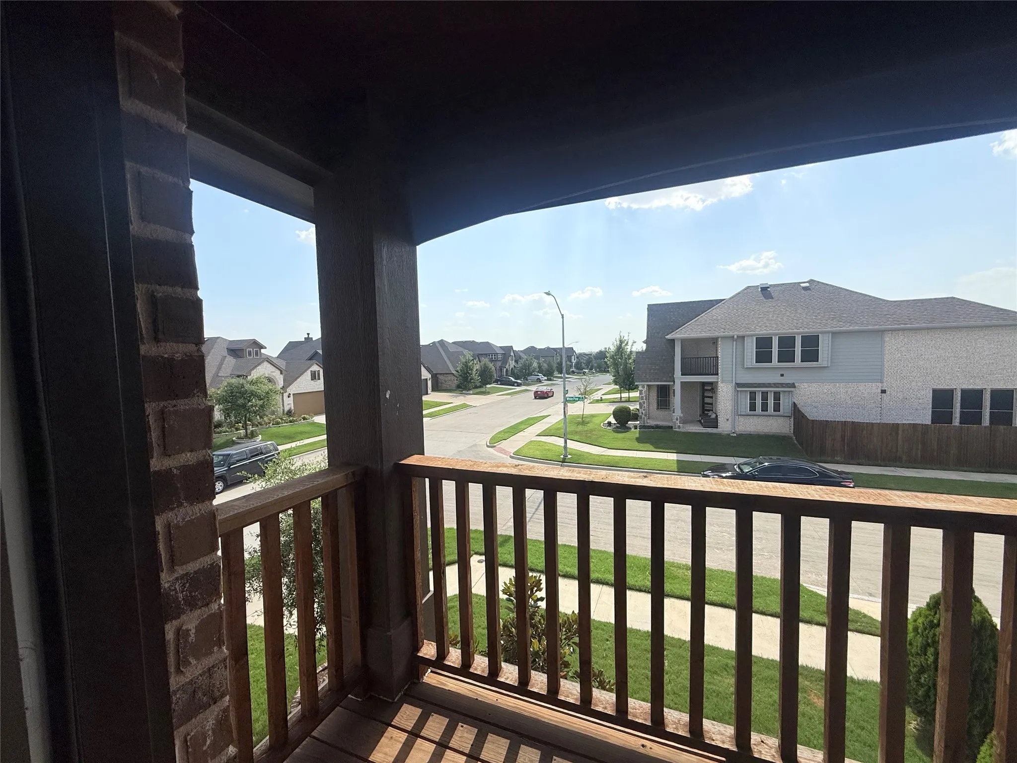 Upper-level balcony featuring wood-finish railings, wood-finish flooring, and brick architectural elements