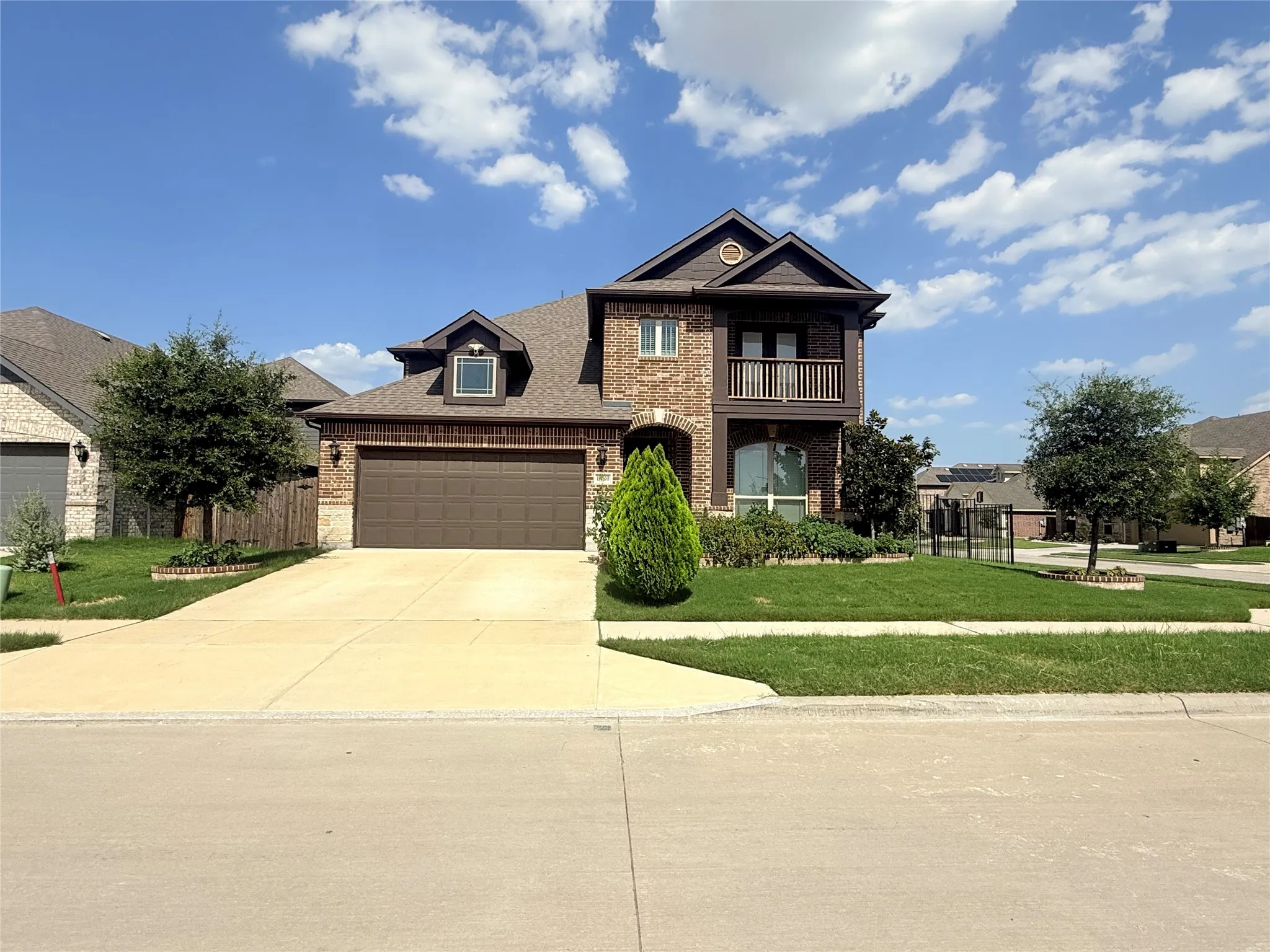 Brick facade home featuring a prominent two-car garage with a brown door, an upper-level balcony, and a dormer window