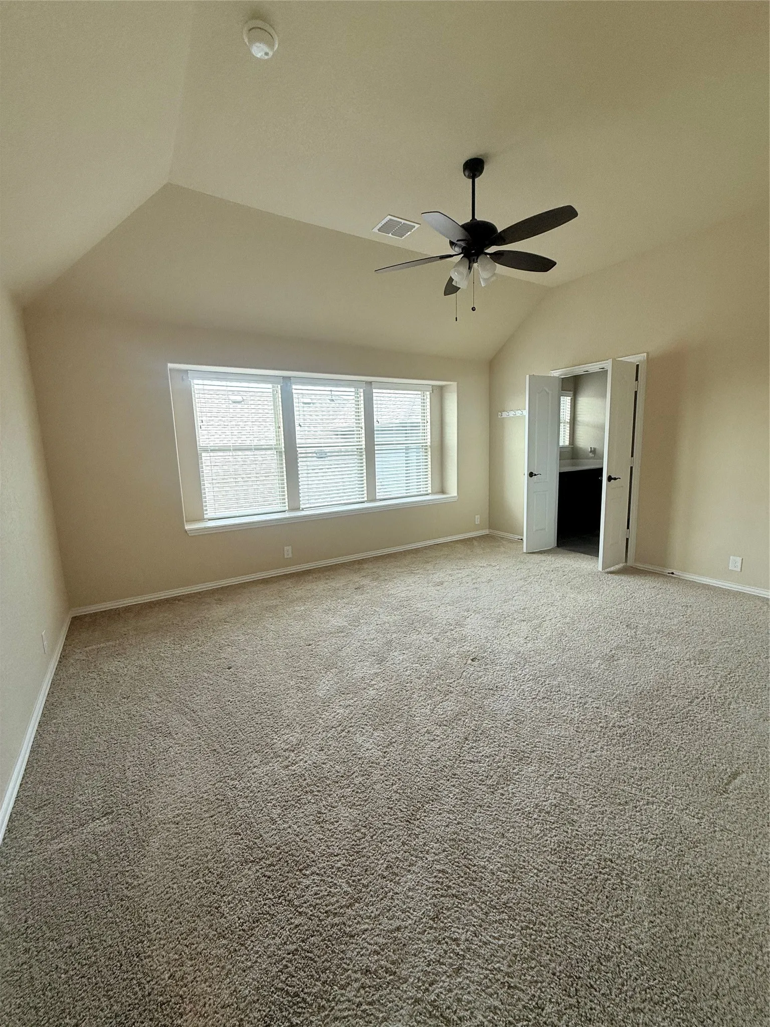 Spacious room featuring vaulted ceilings, a contemporary ceiling fan with integrated lighting, expansive windows with blinds, and neutral-toned carpeting