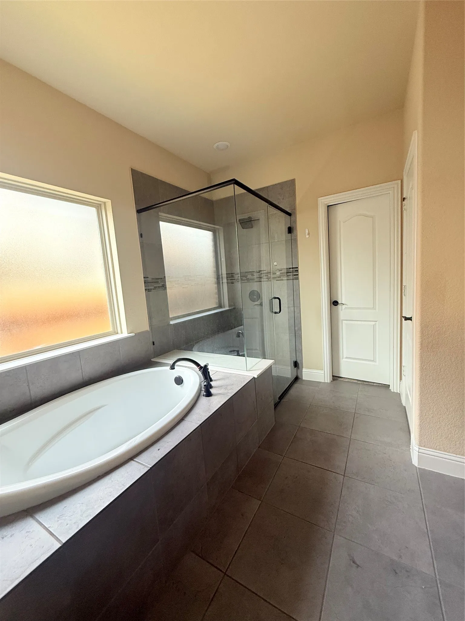 Contemporary bathroom featuring a freestanding oval tub with a black faucet, a glass-enclosed shower with a tiled surround and decorative accent tile, and large format tile flooring