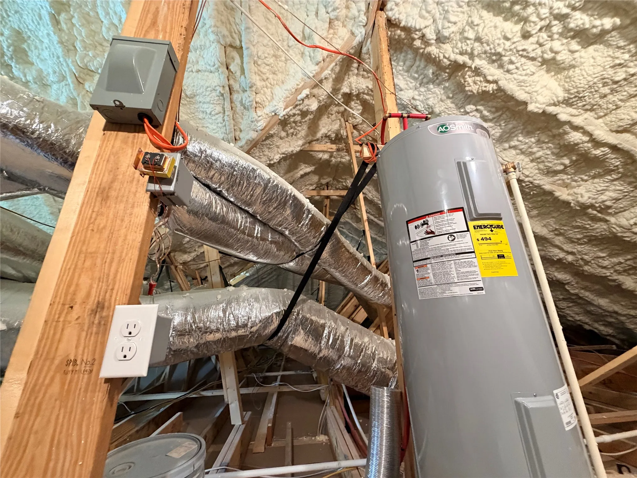 Attic space featuring a water heater, insulated ductwork, and spray foam insulation