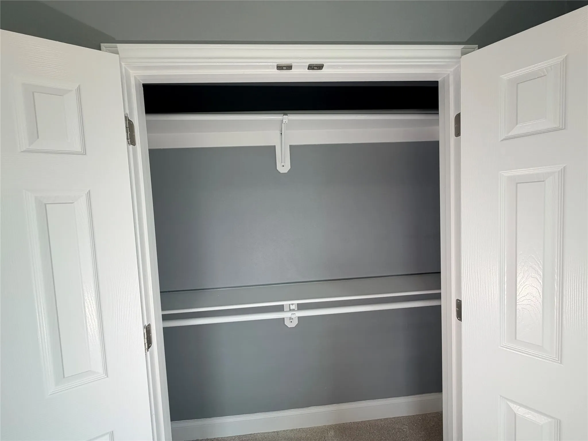 Dual panel doors opening to a closet featuring two storage rods and a top shelf