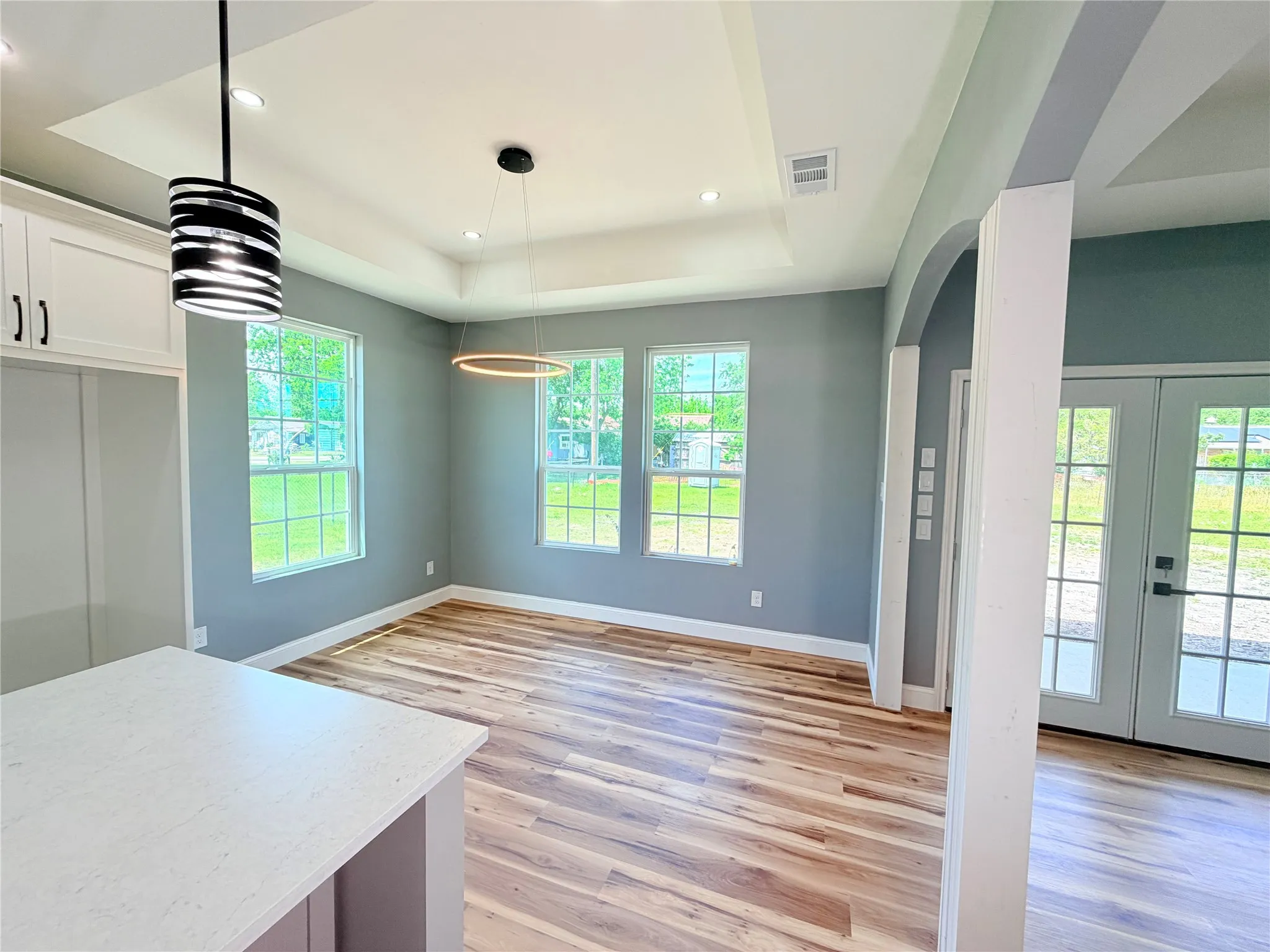 Spacious interior featuring wood-finish flooring, a tray ceiling with recessed lighting, and contemporary pendant fixtures