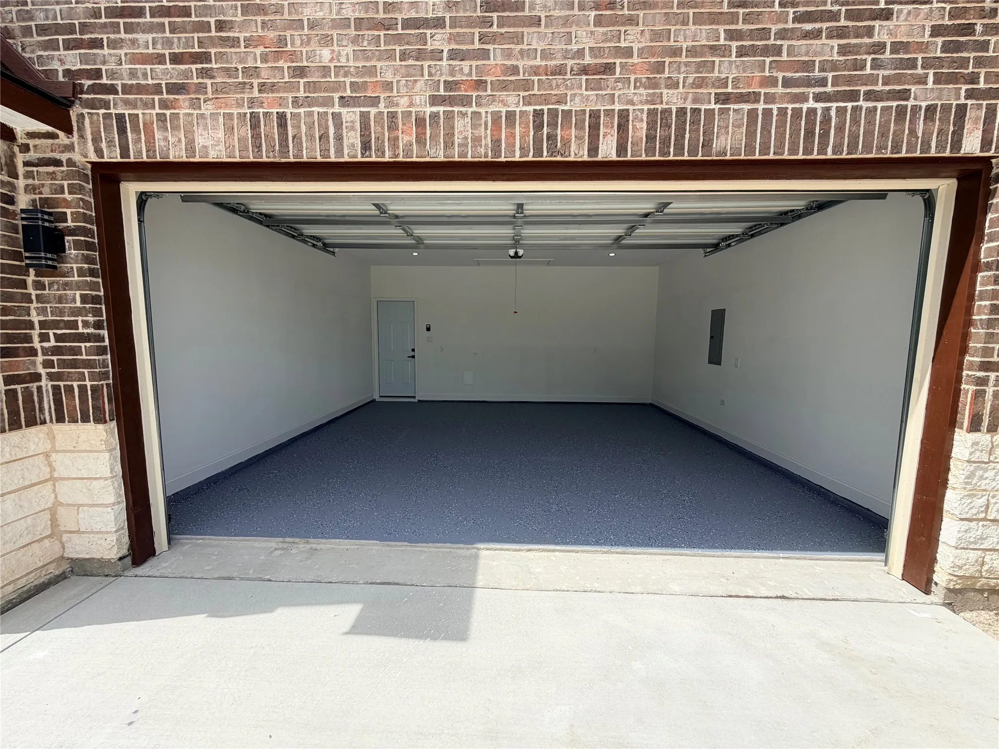 Spacious two-car garage featuring an epoxy-coated concrete floor, white painted walls, and a side access door