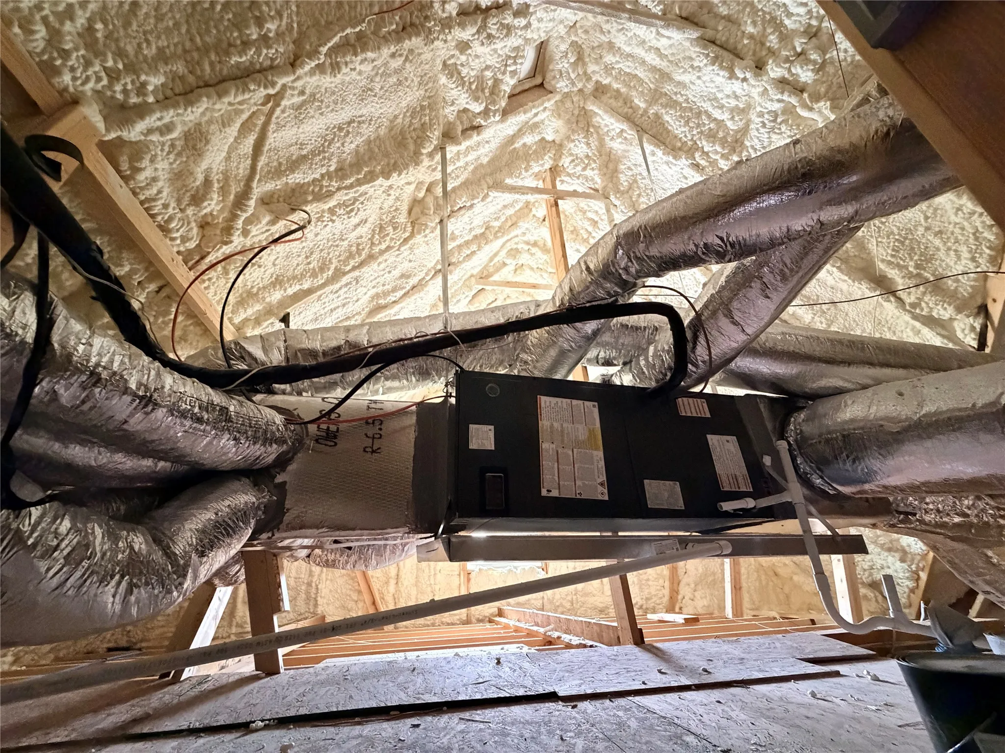 Attic space featuring spray foam insulation, exposed wooden trusses, and installed ductwork