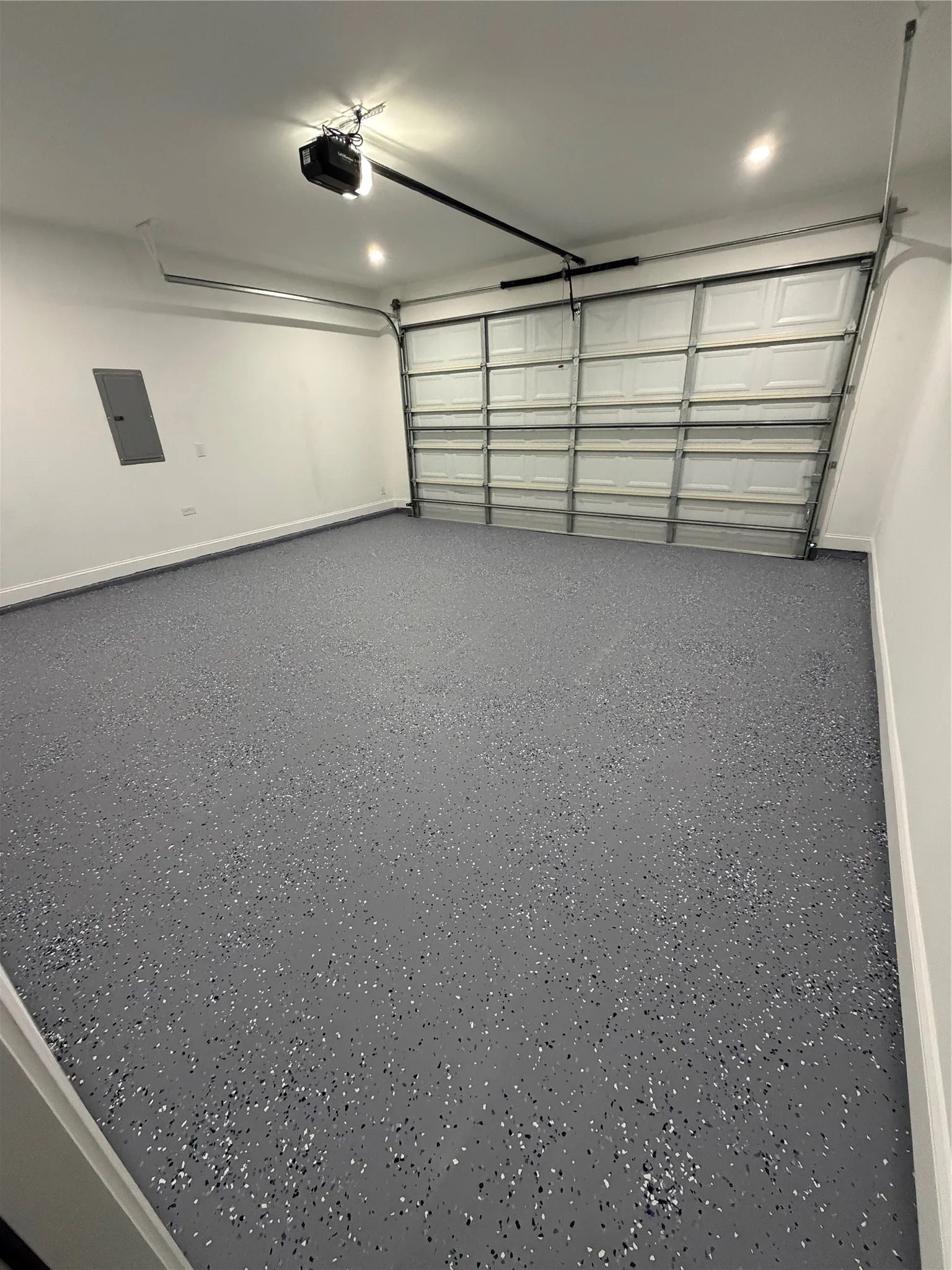 Spacious garage featuring a durable flake epoxy flooring, crisp white walls, recessed lighting, an automatic garage door opener, and a panel box