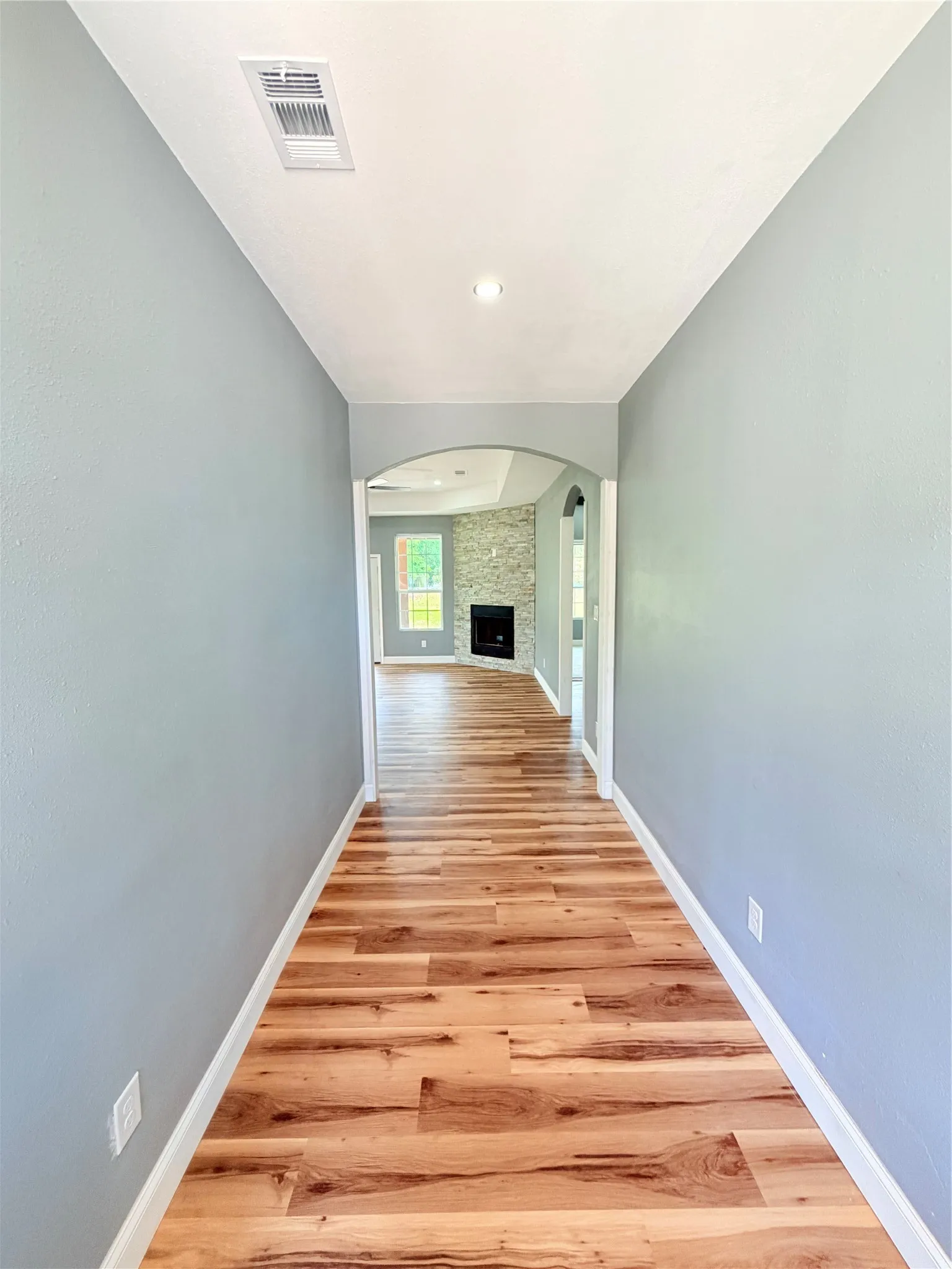 Hallway featuring wood-finish flooring, light blue walls, and white baseboards