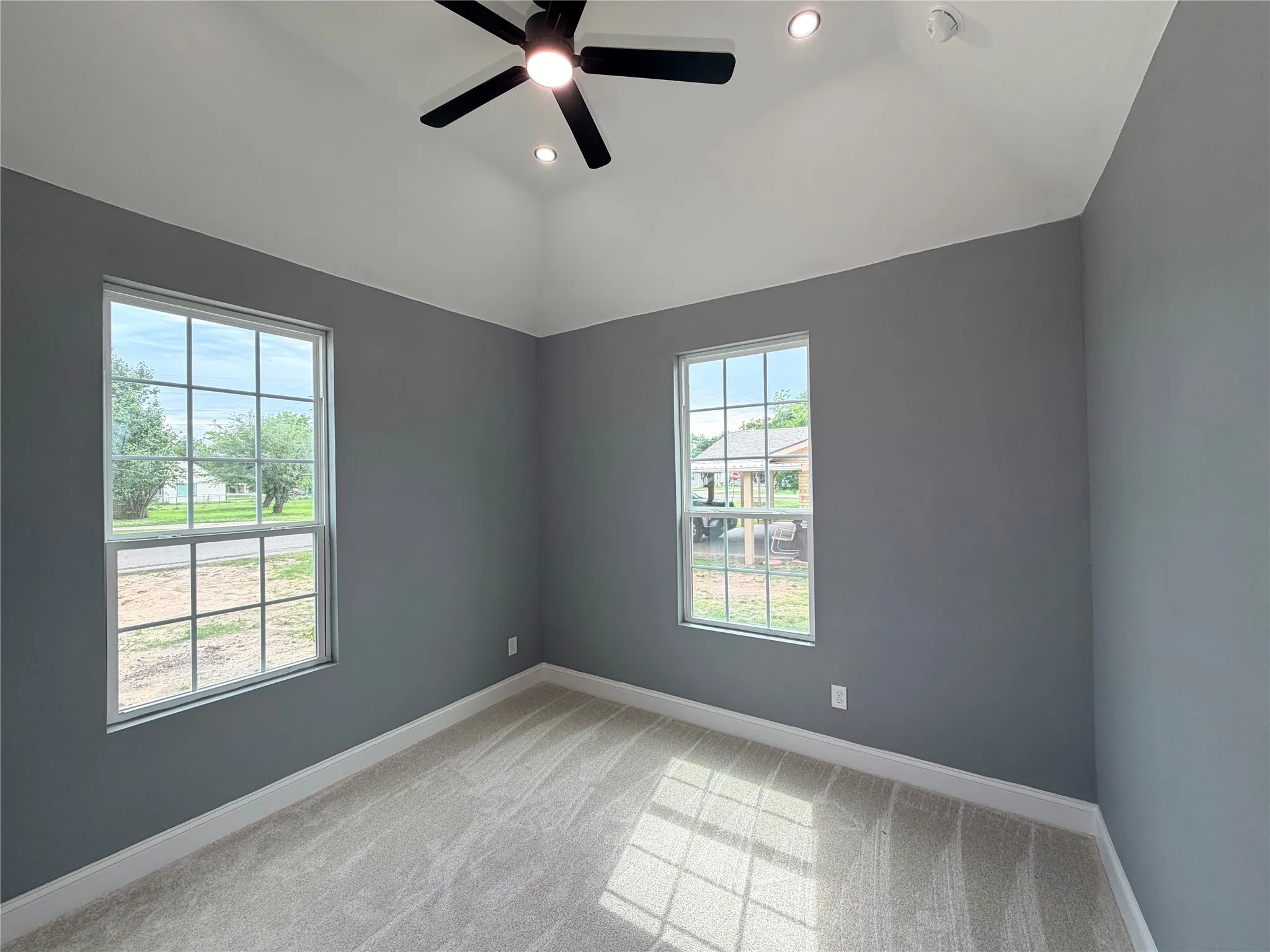 Vaulted ceiling bedroom featuring neutral carpeting, two large windows, a ceiling fan with integrated lighting, and recessed lighting