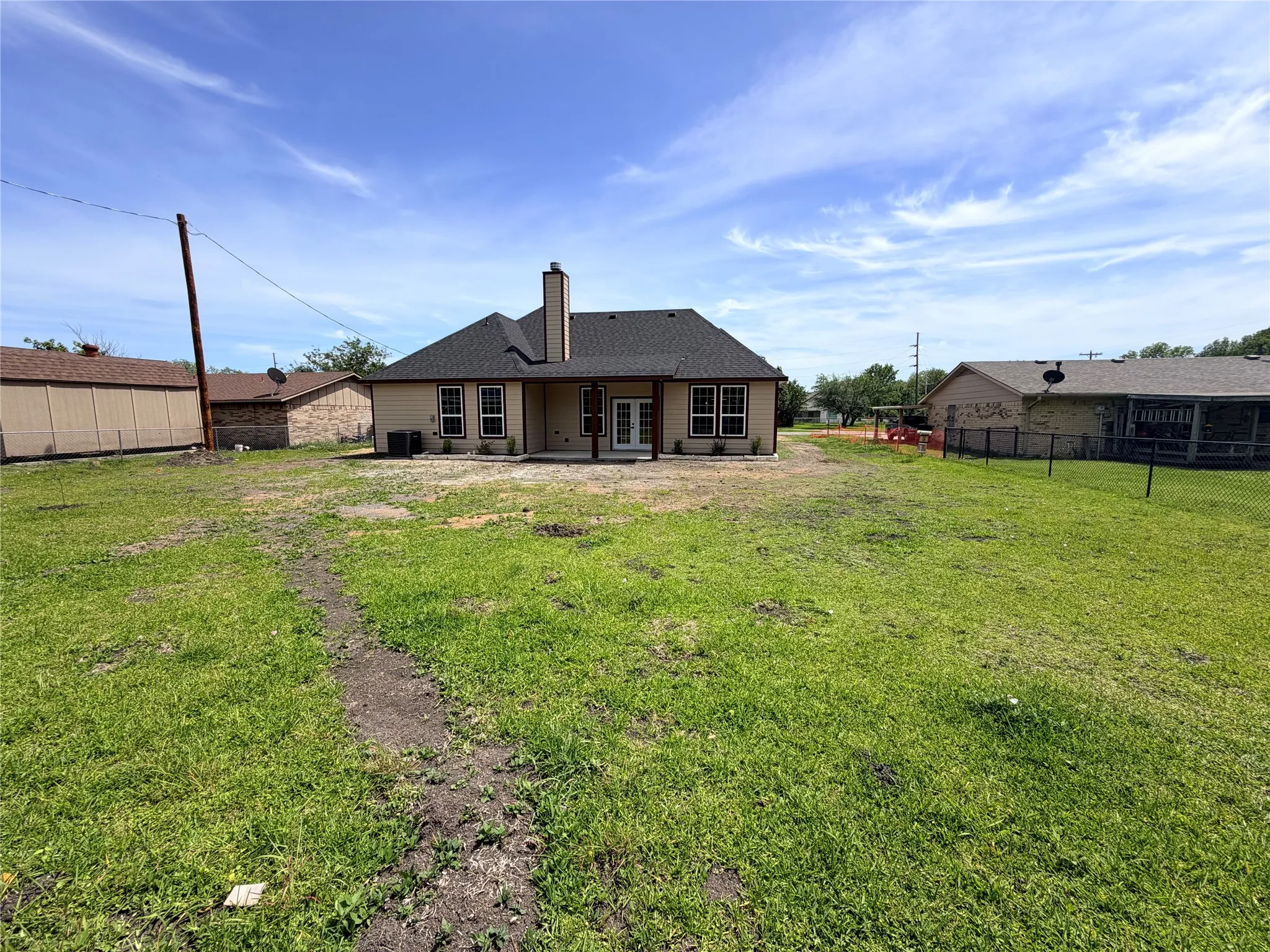 Expansive backyard with a large patio featuring a covered area, two exterior doors, and a central chimney