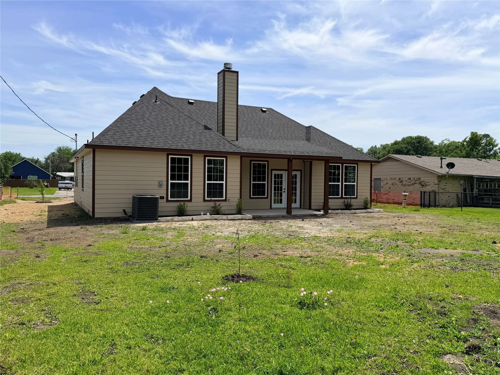 Rear exterior featuring a covered patio, multiple double-hung windows, and a prominent chimney structure