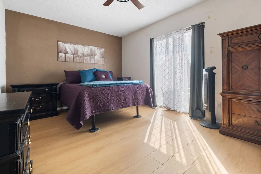 Spacious room featuring wood-finish flooring, a ceiling fan, and a large window with vertical blinds