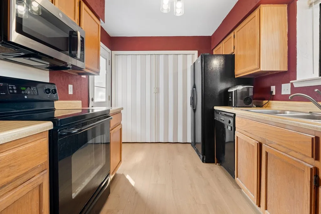 Kitchen featuring wood-finish flooring, wood cabinetry, stainless steel microwave, black electric range, and black dishwasher