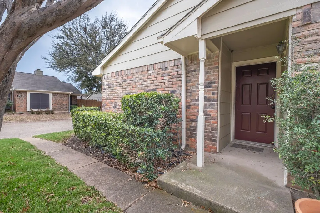 Brick and siding exterior featuring a covered entryway with a paneled front door, an established shrub border, and a concrete walkway