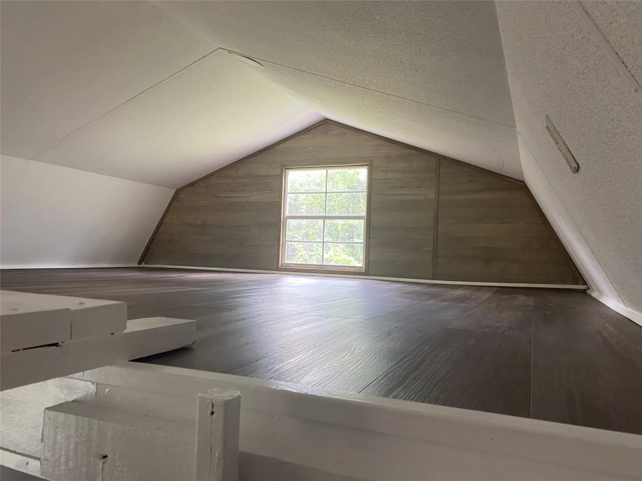 Loft space bedroom featuring dark wood-finish flooring, a white-framed window, and sloped white ceilings