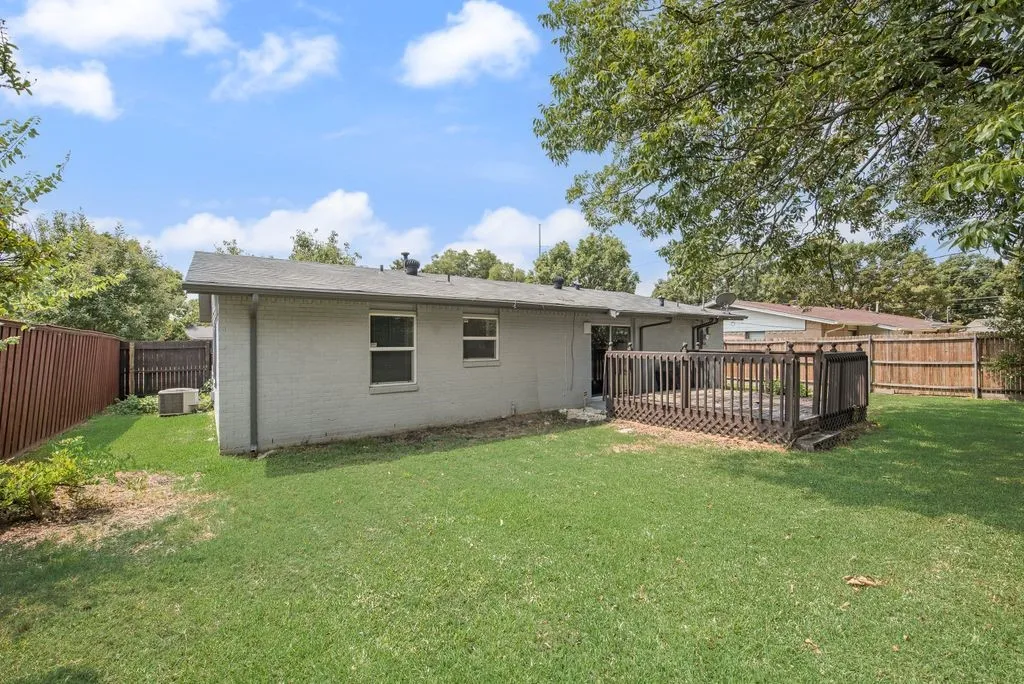 Expansive rear yard featuring a large wood deck, mature trees providing natural shade, and privacy fencing