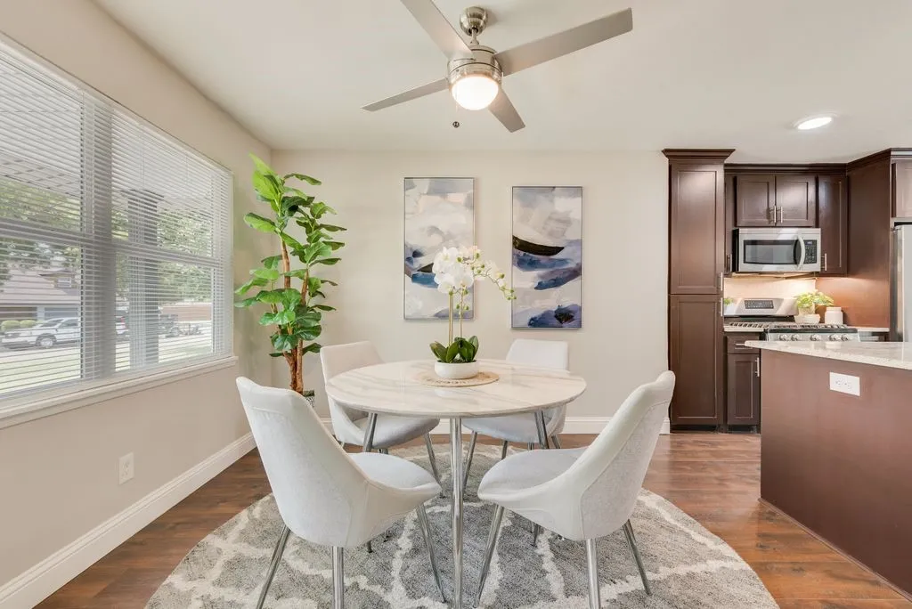 Bright dining area featuring a round pedestal table with seating for four, positioned beneath dual abstract artwork and a ceiling fan