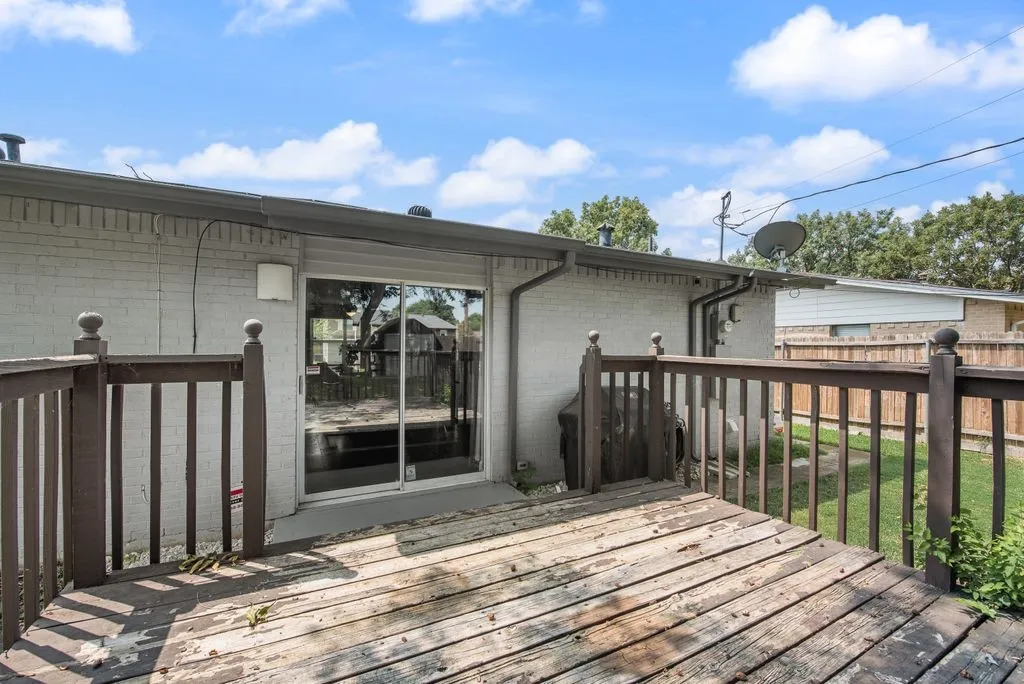 Exterior wooden deck featuring a full-length sliding glass door, white brick siding, and a wooden privacy fence