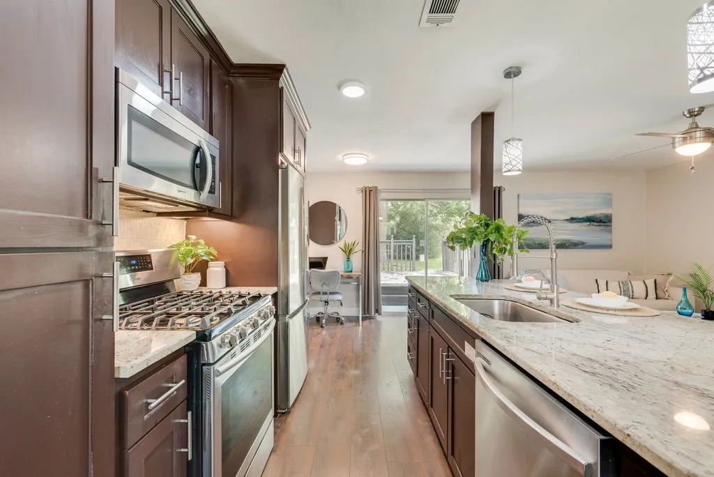 Kitchen featuring a substantial island with a stainless steel sink, granite-finish countertops, and under-cabinet lighting