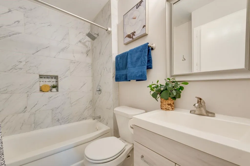 Bright and functional bathroom featuring marble-look tile walls with integrated shower surround, white vanity with ample countertop storage, and brushed nickel fixtures