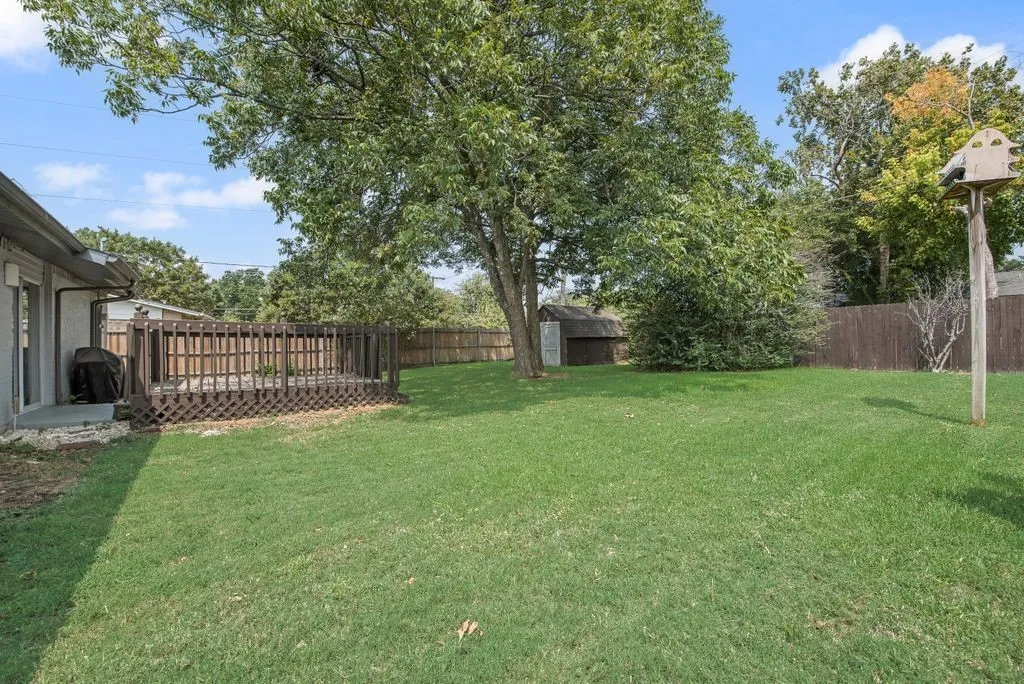 Expansive lawn area featuring a wooden privacy fence and mature trees