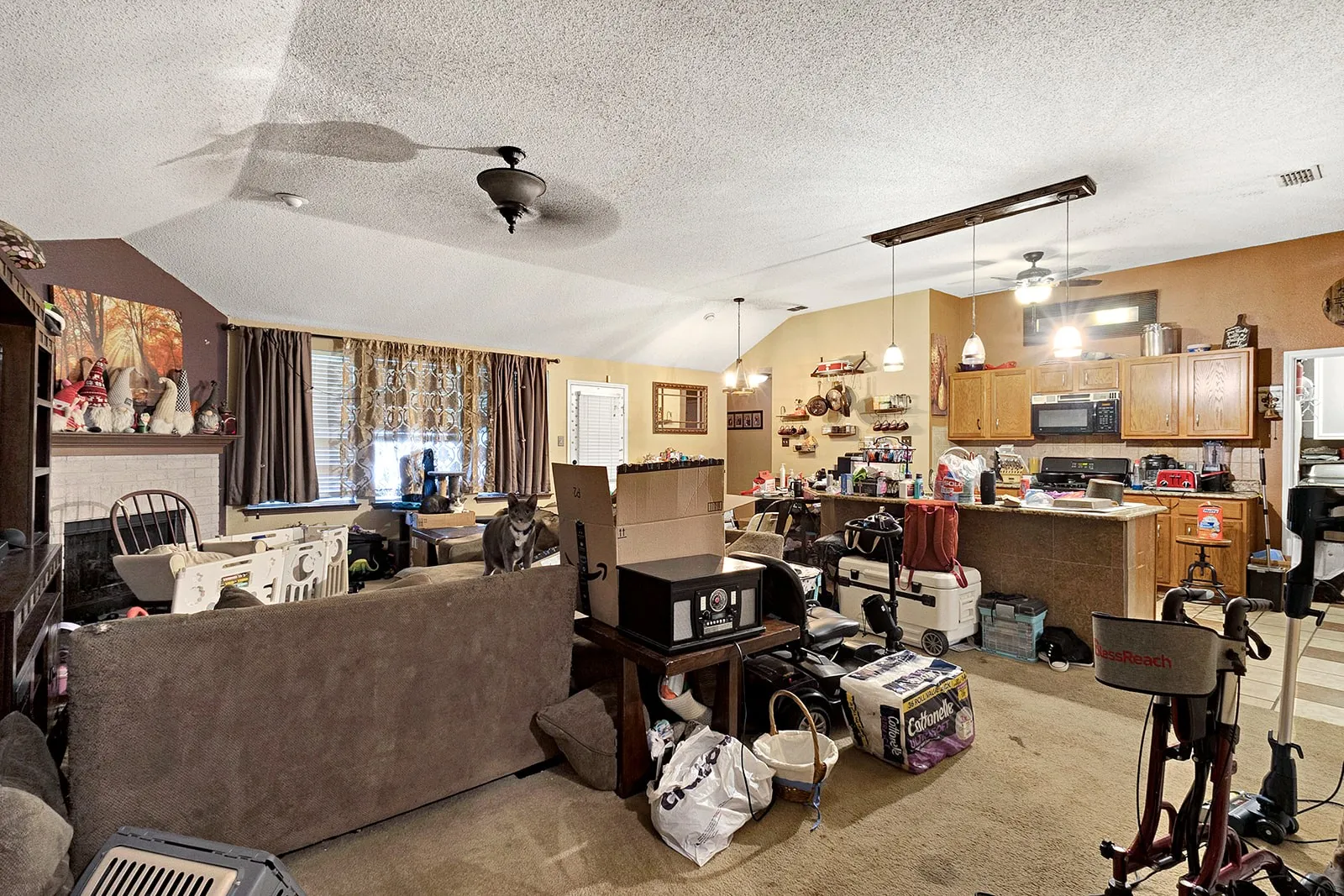 Vaulted living area featuring a fireplace with mantel, ceiling fan, and window treatments