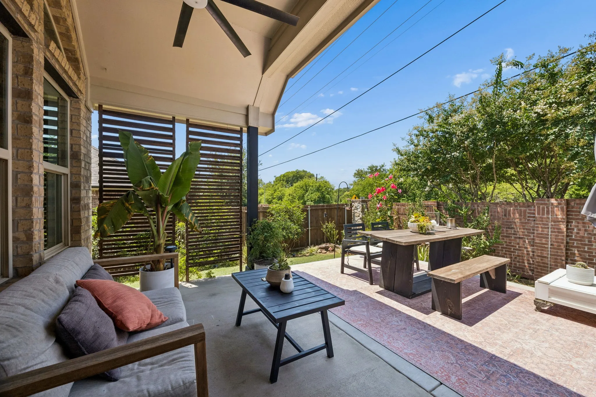 Beautiful covered patio with privacy screen, ceiling fan and lush greenery