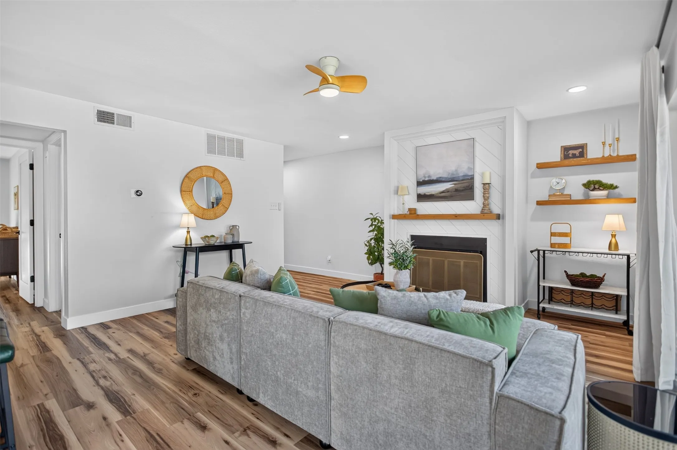 Living area featuring wood-finish flooring, a white fireplace with a wood mantel, and built-in wood floating shelves