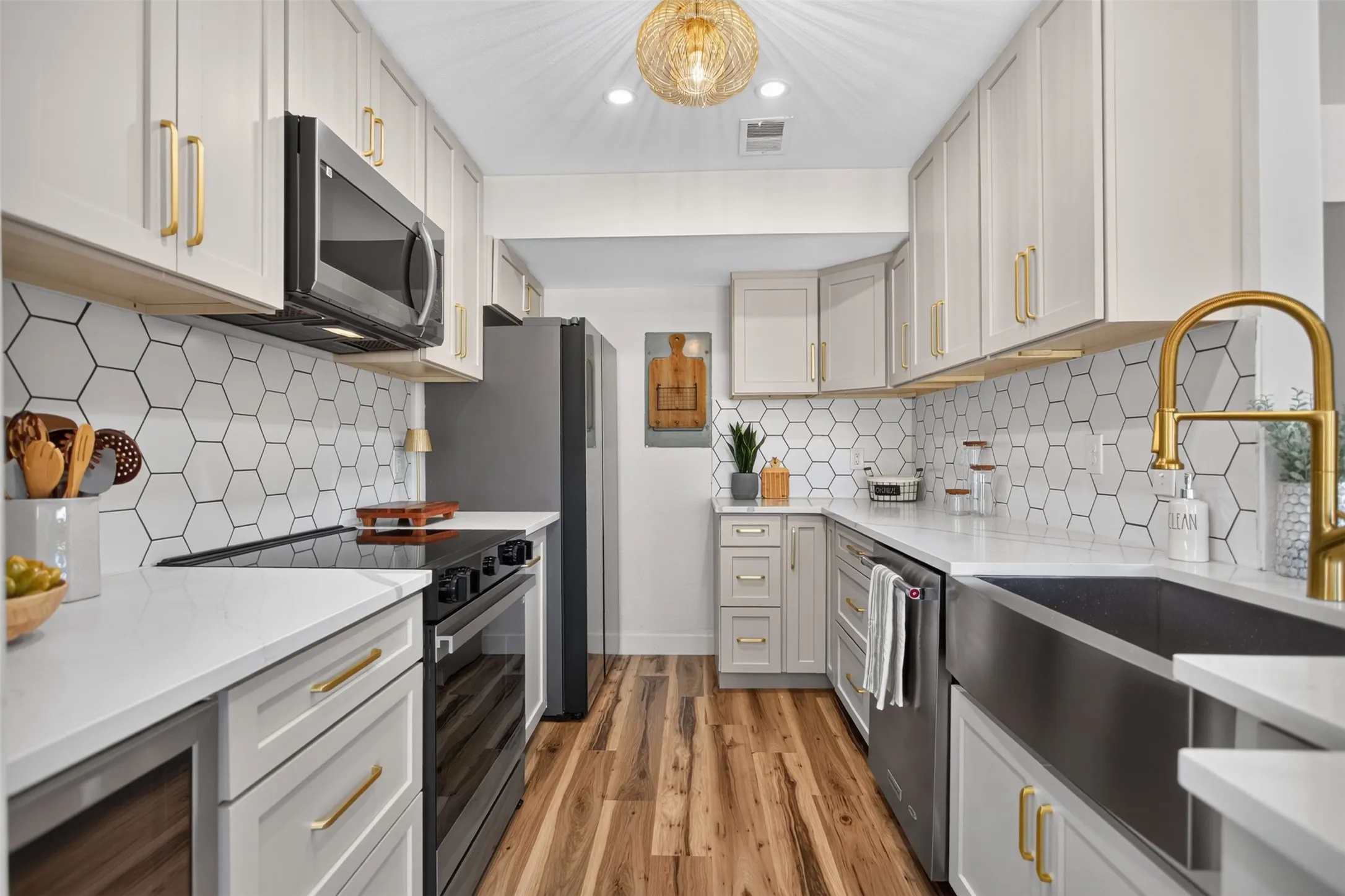 Contemporary kitchen featuring white shaker-style cabinetry, gold-finish hardware, hexagon tile backsplash, quartz countertops, and wood-finish flooring