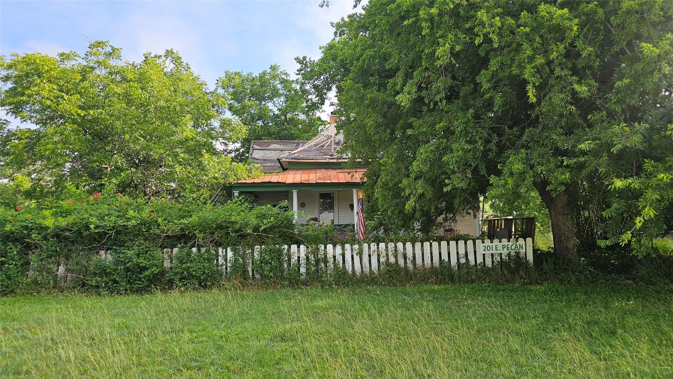 Residential structure with a front porch and a white picket fence, set amidst mature trees and natural landscaping