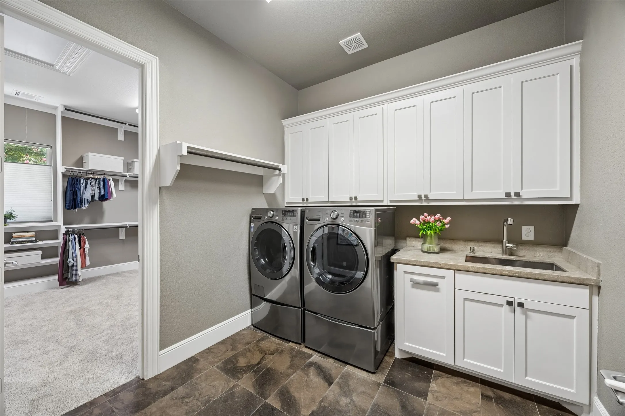 Laundry room featuring tile flooring, white shaker cabinetry, a built-in sink with a countertop, and a clothes hanging rod