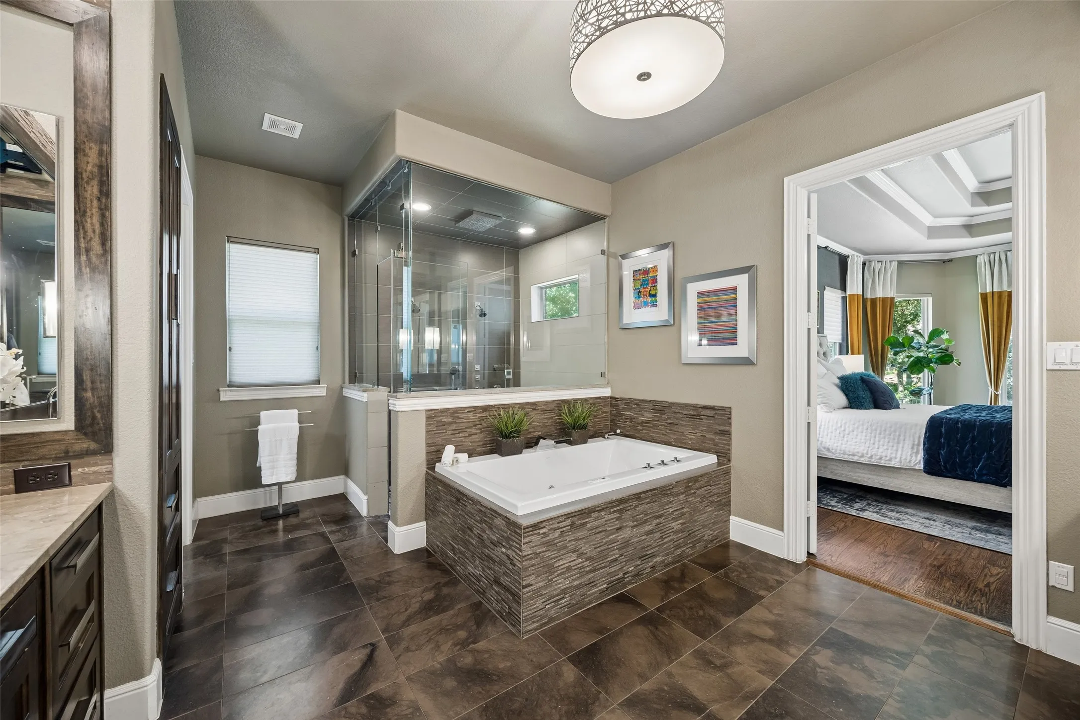 Spacious bathroom featuring a built-in jetted tub with stone-finish surround, a glass-enclosed shower, a double vanity with stone countertops, and dark-finish tile flooring