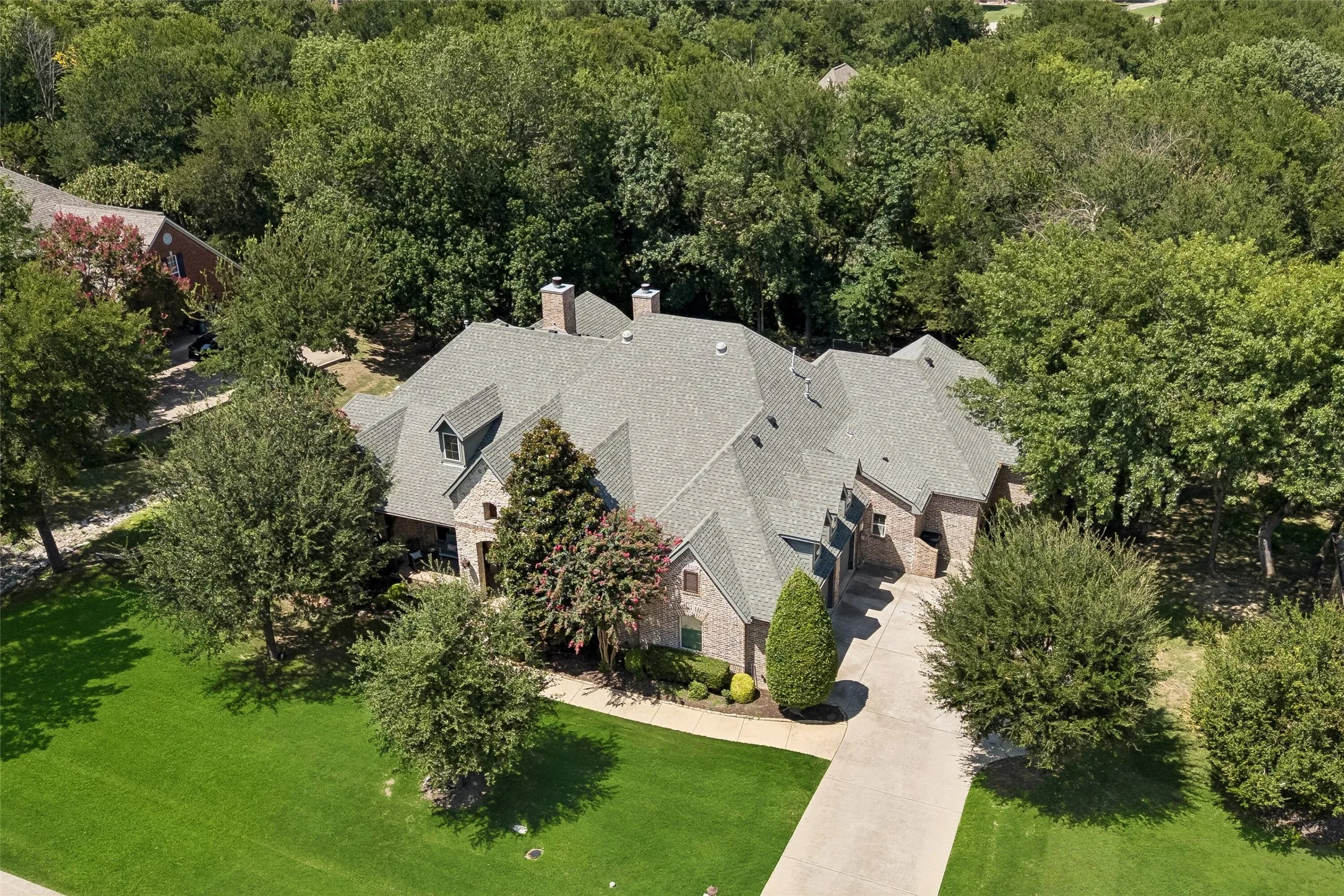 Expansive brick and stone residence featuring a multi-gabled roofline, dormer windows, and a generous front lawn