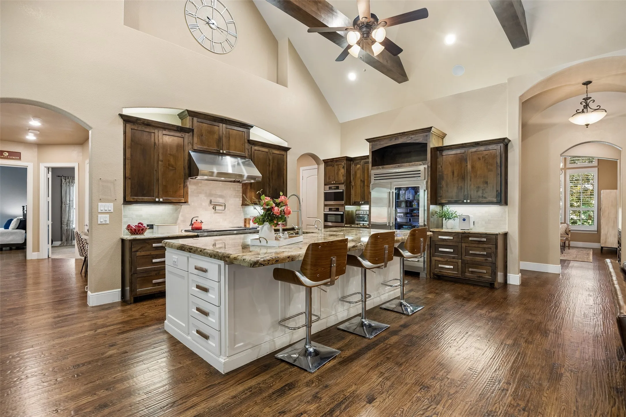 Kitchen featuring a granite-topped island with seating, dark wood cabinetry, stainless steel appliances, wood-finish flooring, and a vaulted ceiling with exposed beams