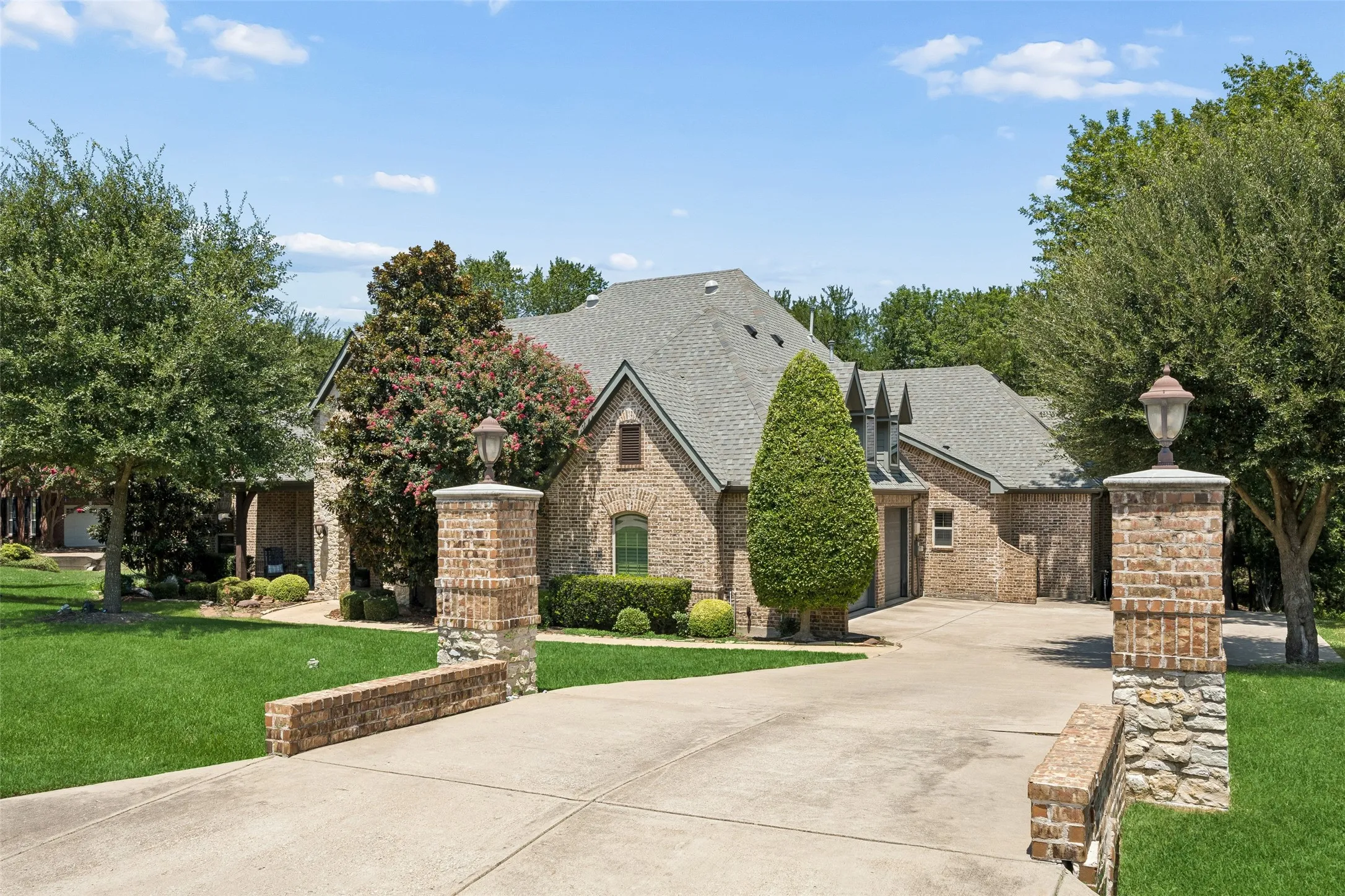 Brick and stone facade residence featuring a concrete driveway, mature landscaping, and an integrated garage