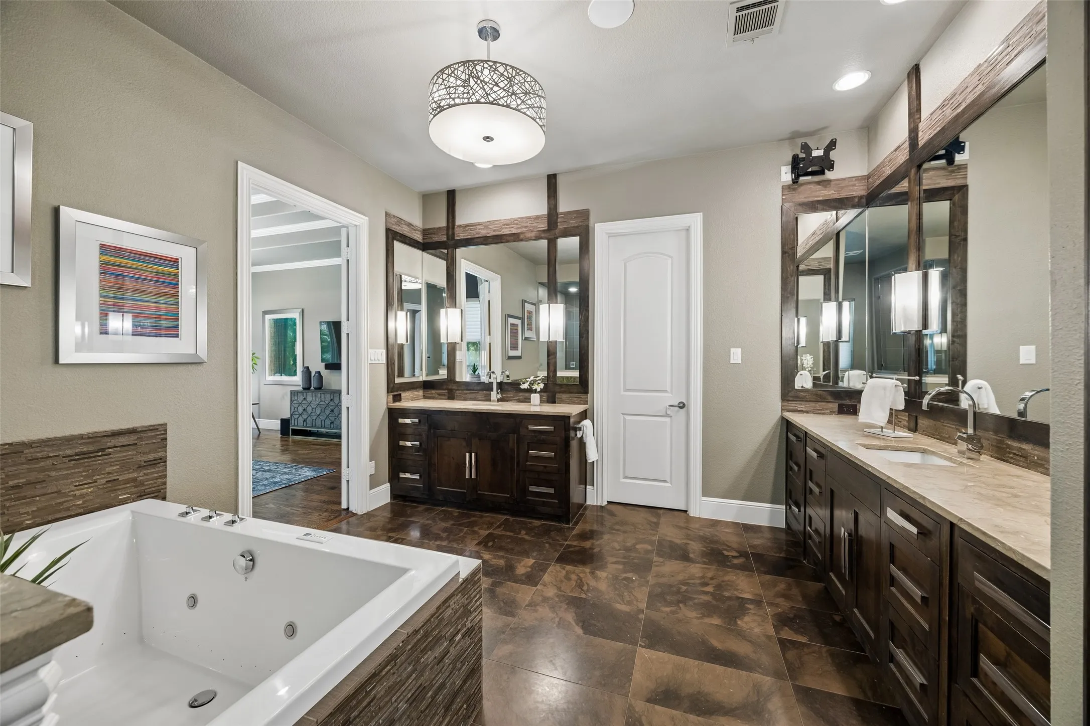Spacious bathroom featuring a deep soaking tub, dual vanity areas with extensive cabinetry, stone countertops, and large framed mirrors