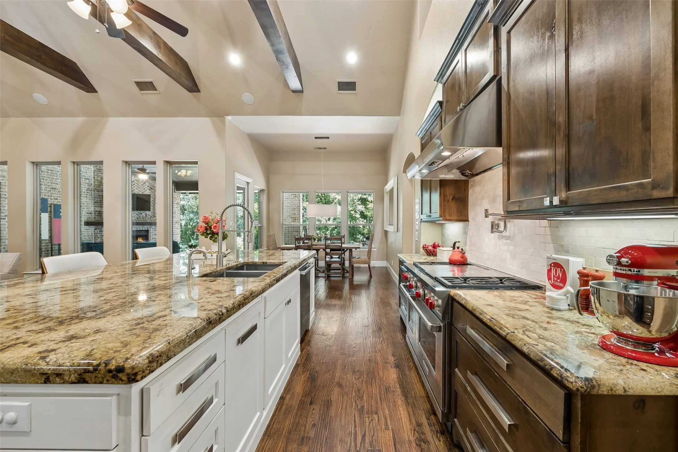 Spacious kitchen featuring a large island with an undermount sink, granite countertops, wood-finish flooring, dark wood cabinetry, and a stainless steel range with a ventilation hood