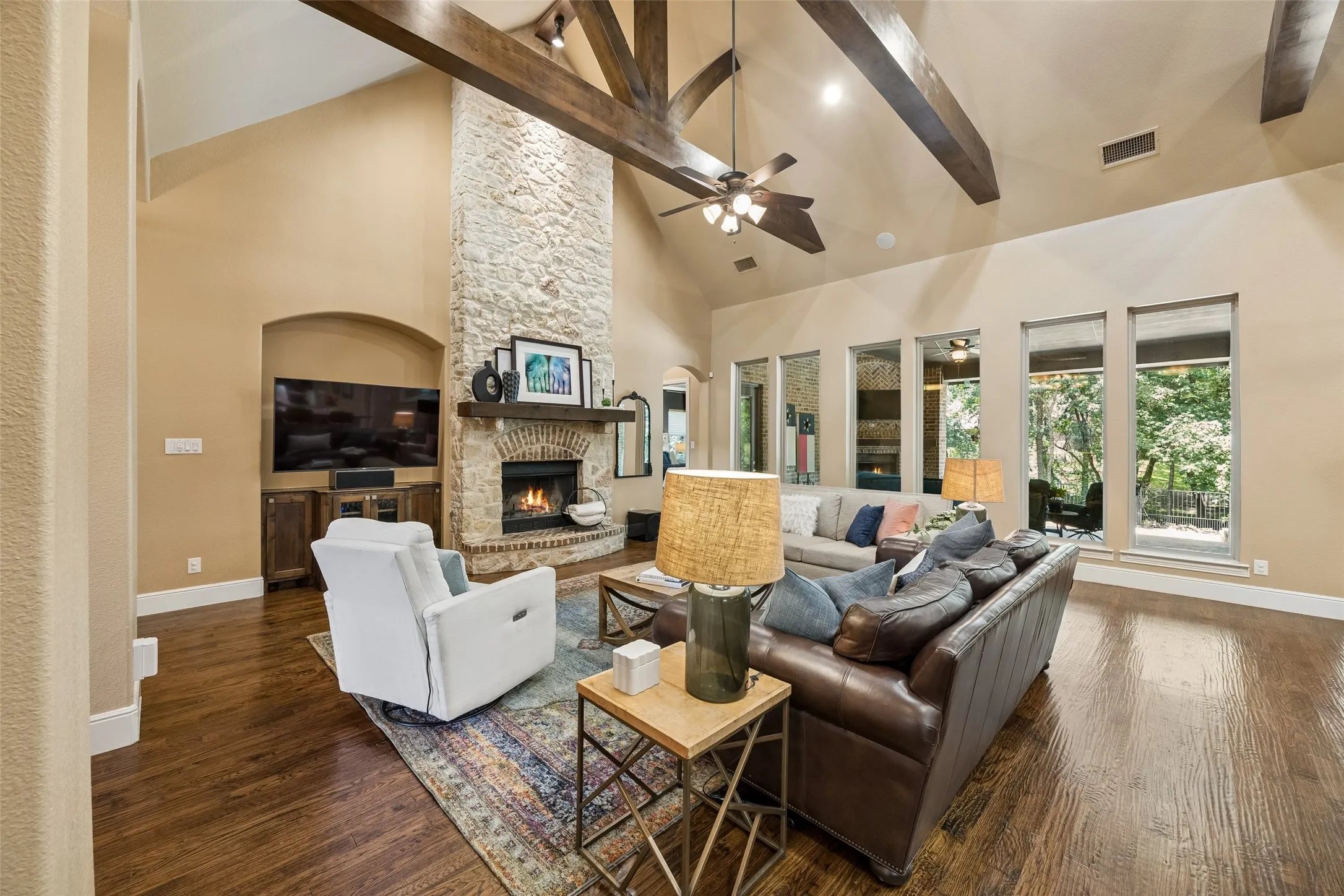 Vaulted ceilings with exposed wood beams, a floor-to-ceiling stone fireplace, large windows, and dark wood-finish flooring