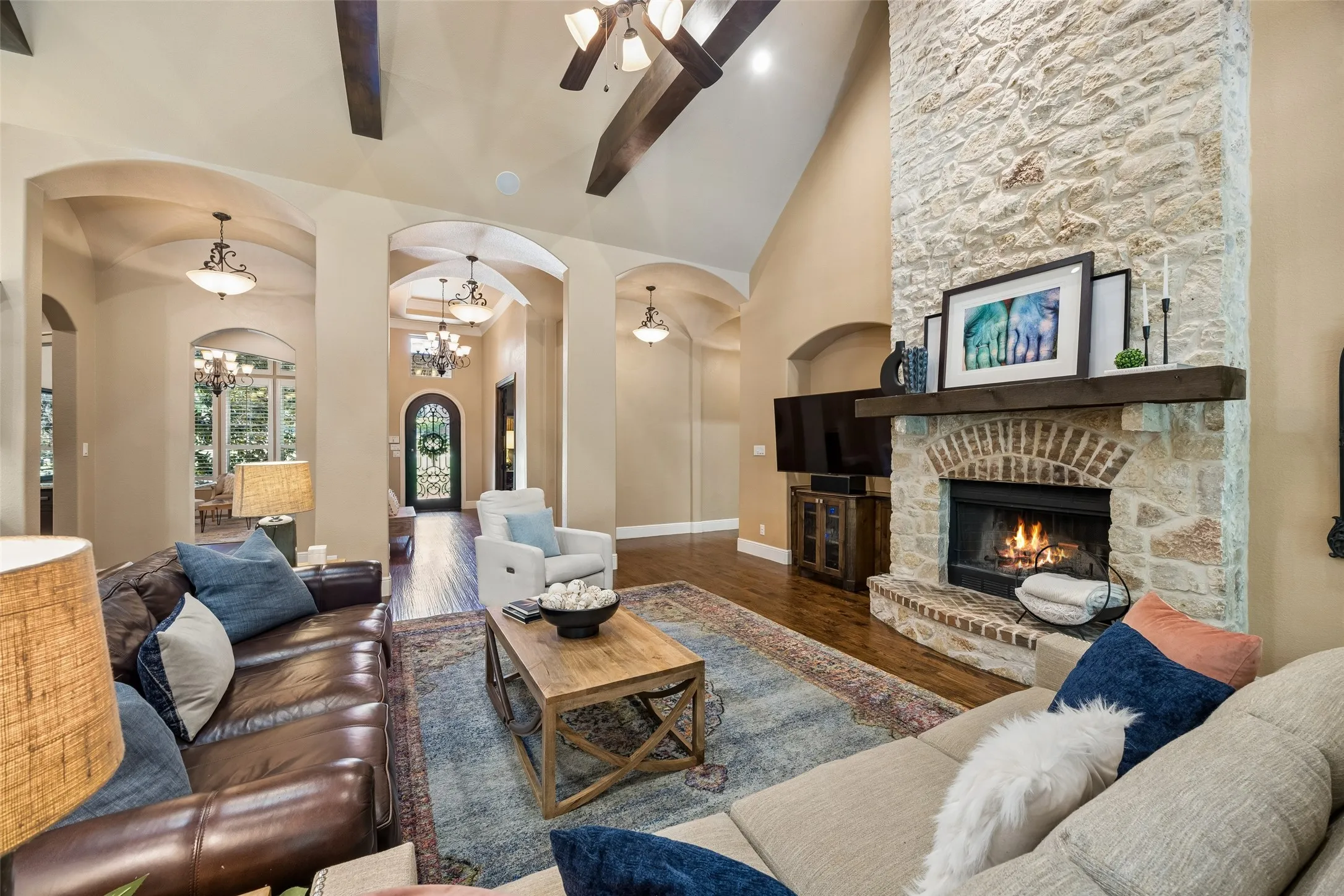 Expansive living area featuring a stone fireplace with a brick arch and wood mantel