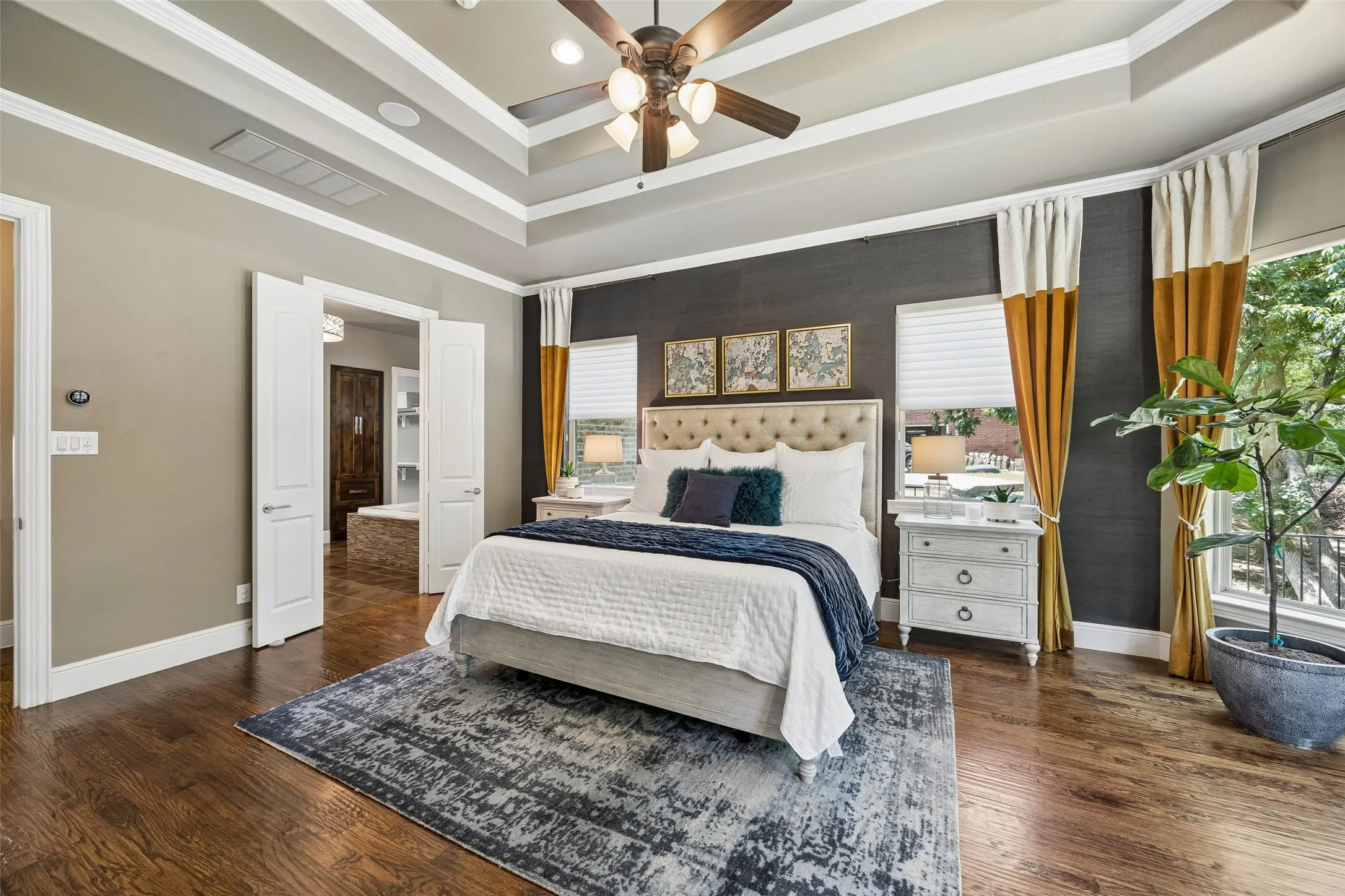 Spacious room featuring rich wood-finish flooring, a tiered tray ceiling, and a ceiling fan