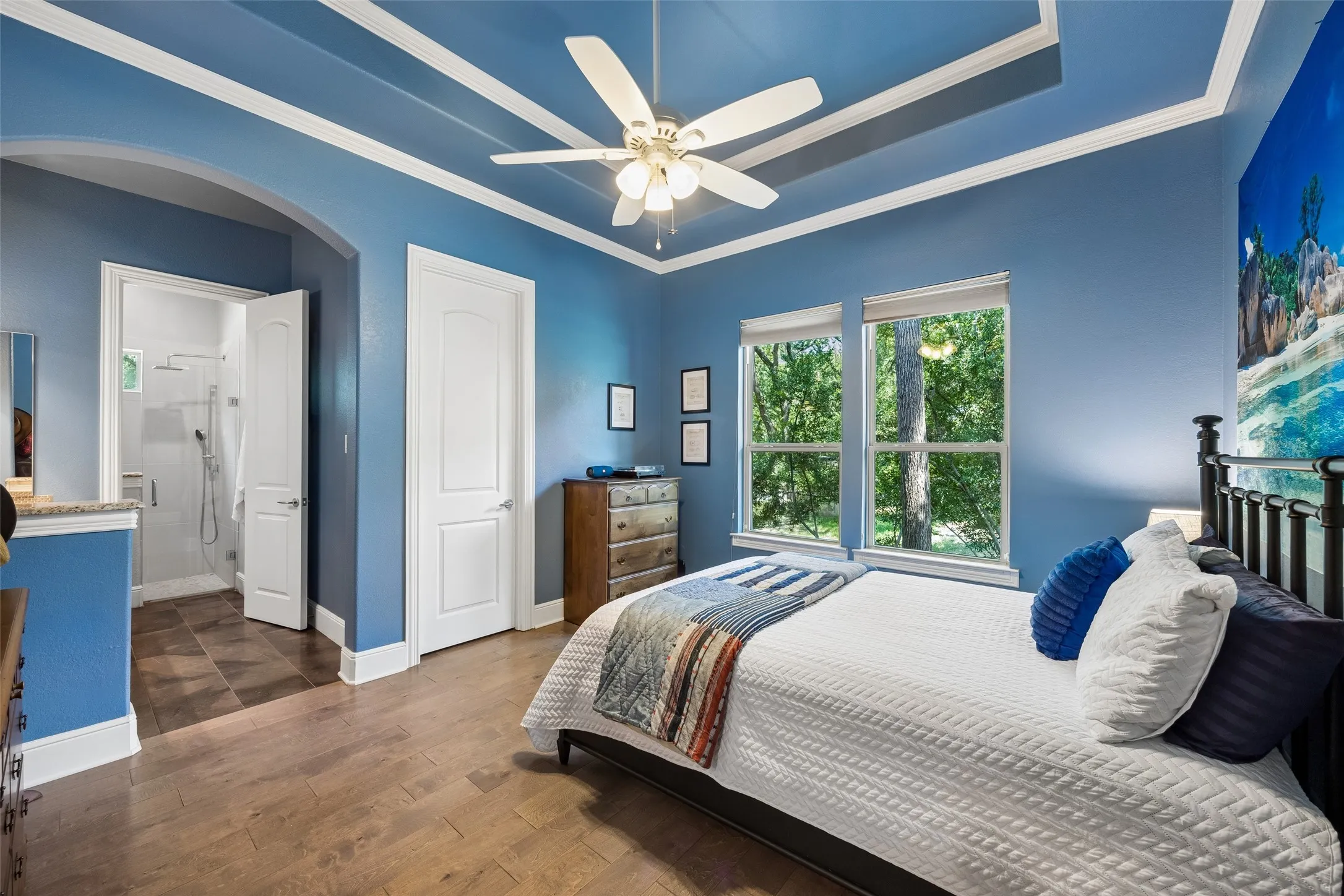 Bedroom featuring wood-finish flooring, a tray ceiling with crown molding, and a ceiling fan