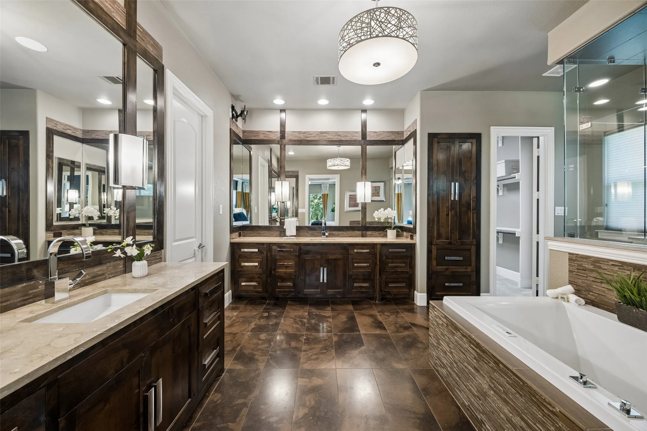 Spacious bathroom featuring dual vanities with light-toned countertops, dark wood cabinetry, and large mirrors