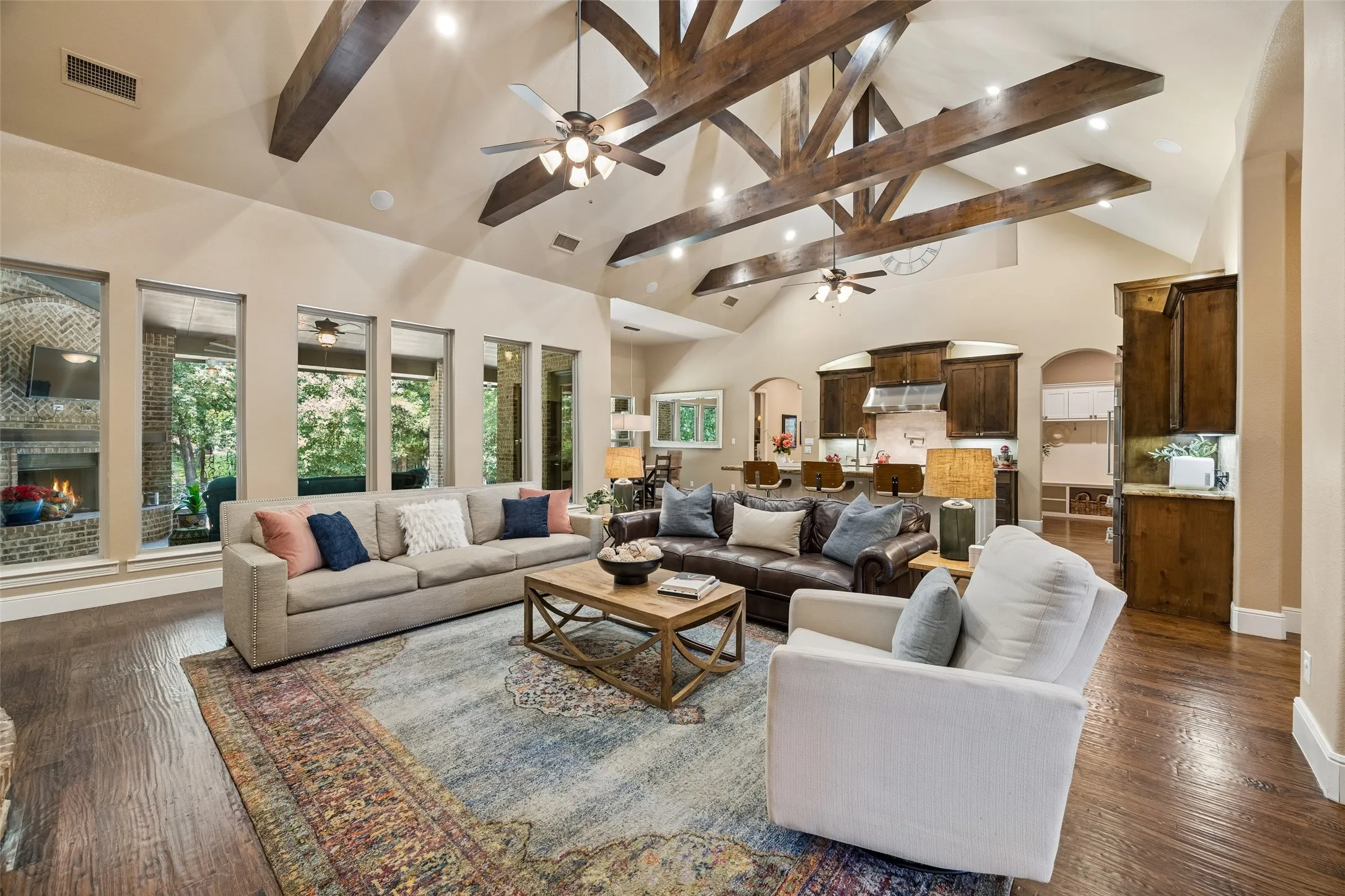 Open-concept living area featuring a vaulted ceiling with exposed wood beams, recessed lighting, and ceiling fans