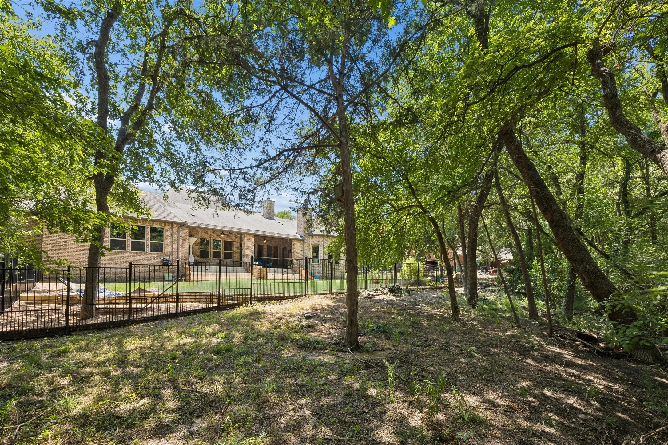 Brick exterior property featuring a fenced backyard, mature trees, an outdoor patio, and multiple windows