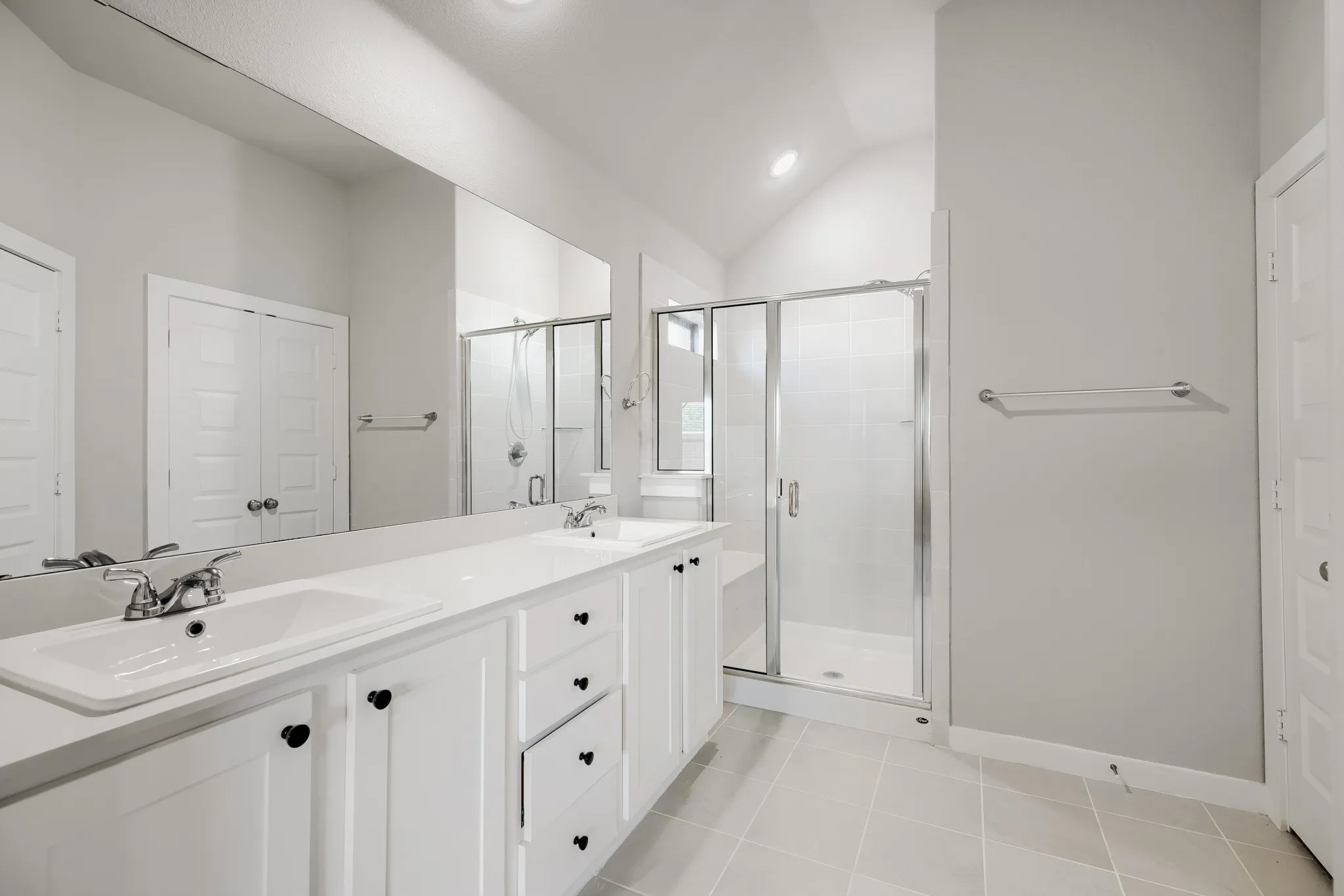 Bright bathroom featuring a dual vanity with white cabinetry, light-colored countertops, and chrome fixtures