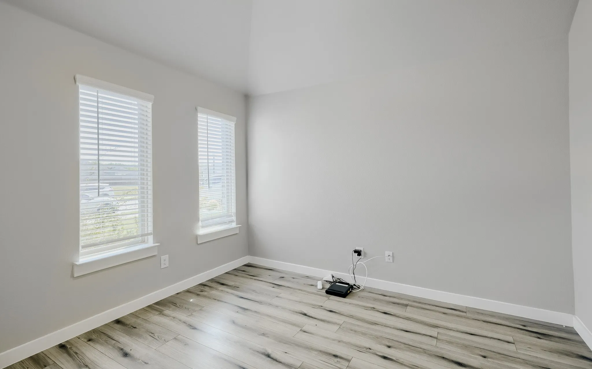 Spacious room featuring light wood-finish flooring, neutral gray walls, and white baseboards