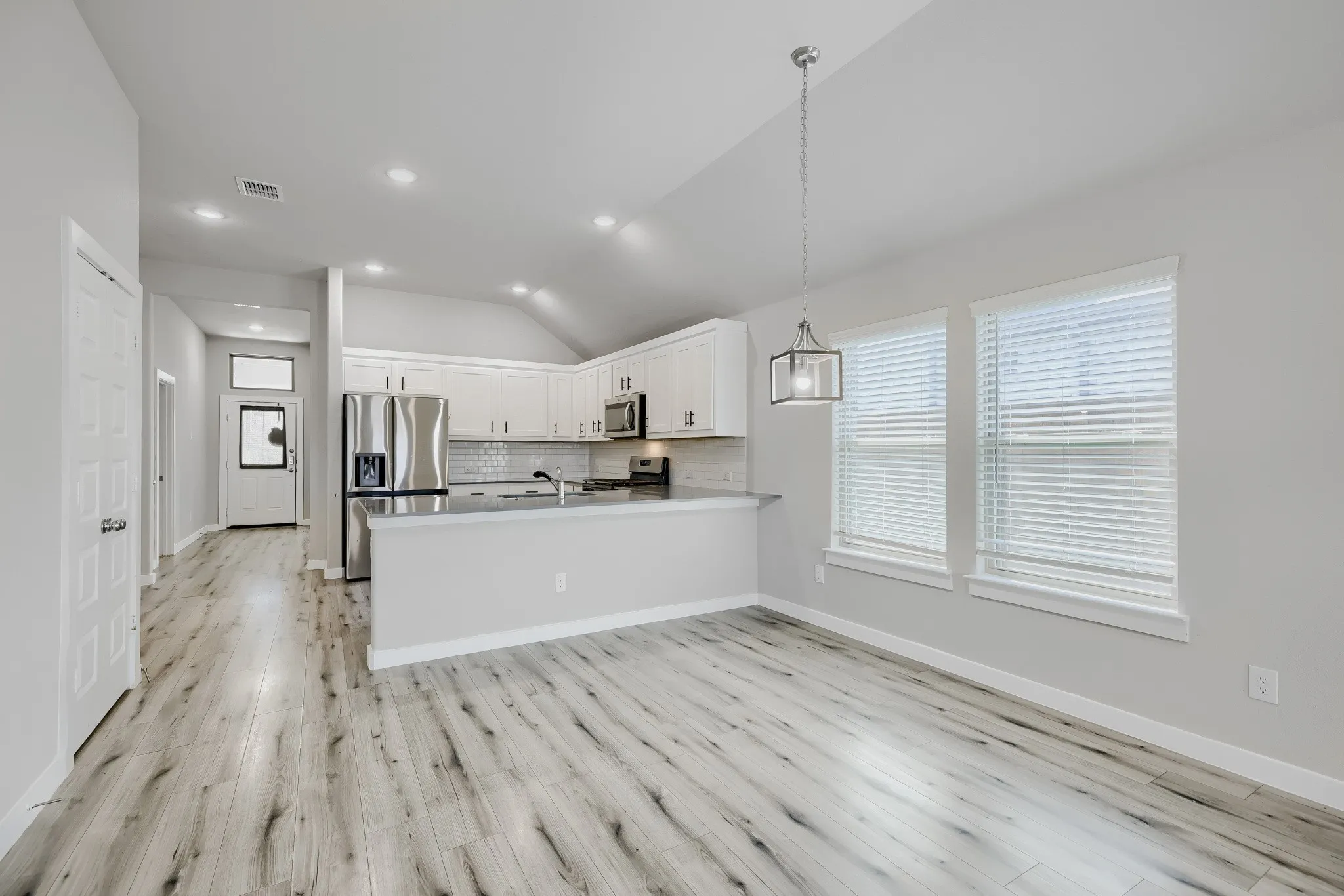 Open-concept living area with high ceilings, wood-finish flooring, and ample natural light from multiple windows