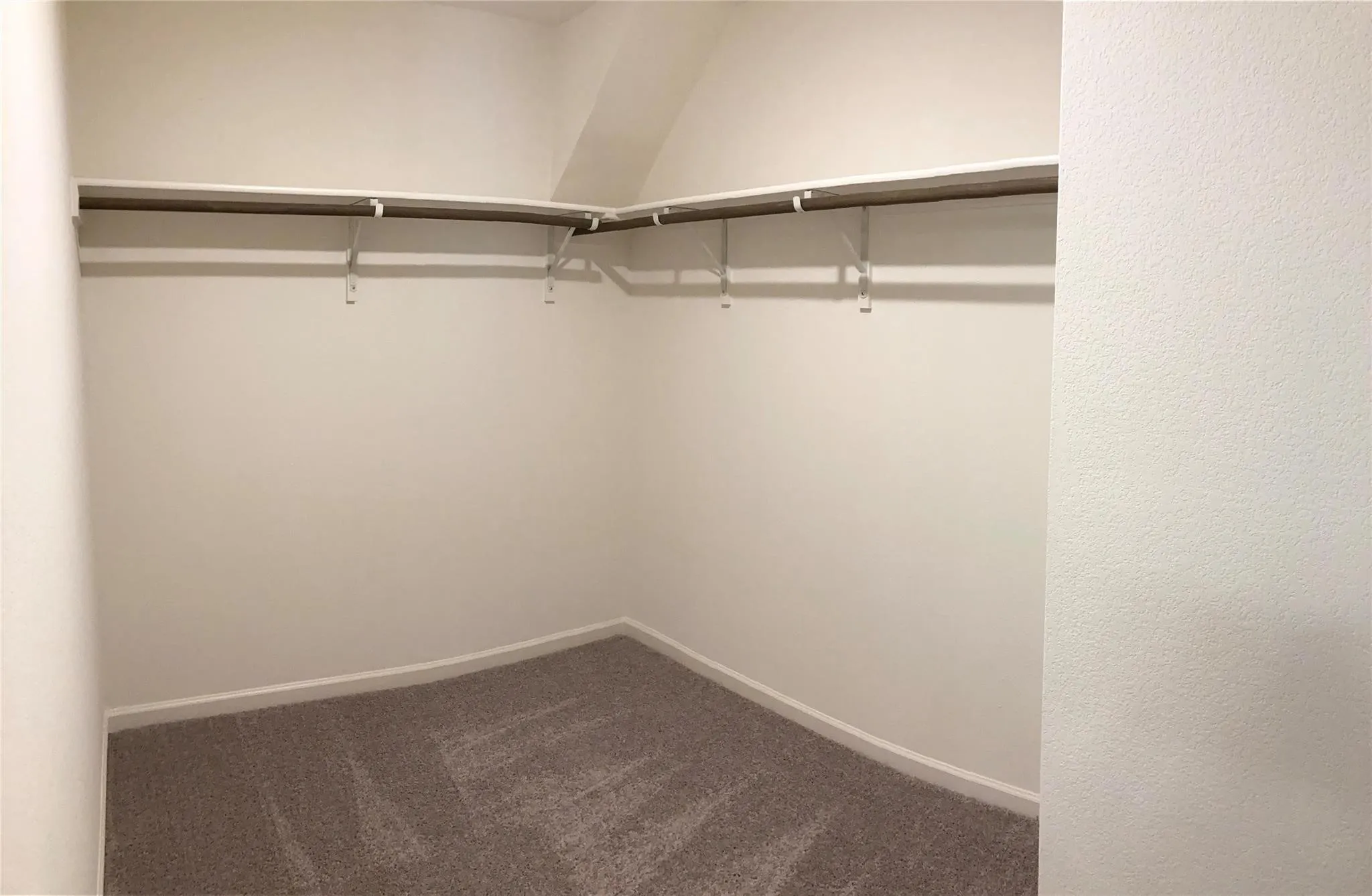 Walk-in closet featuring light gray carpeting, white baseboards, and built-in white shelving with hanging rods