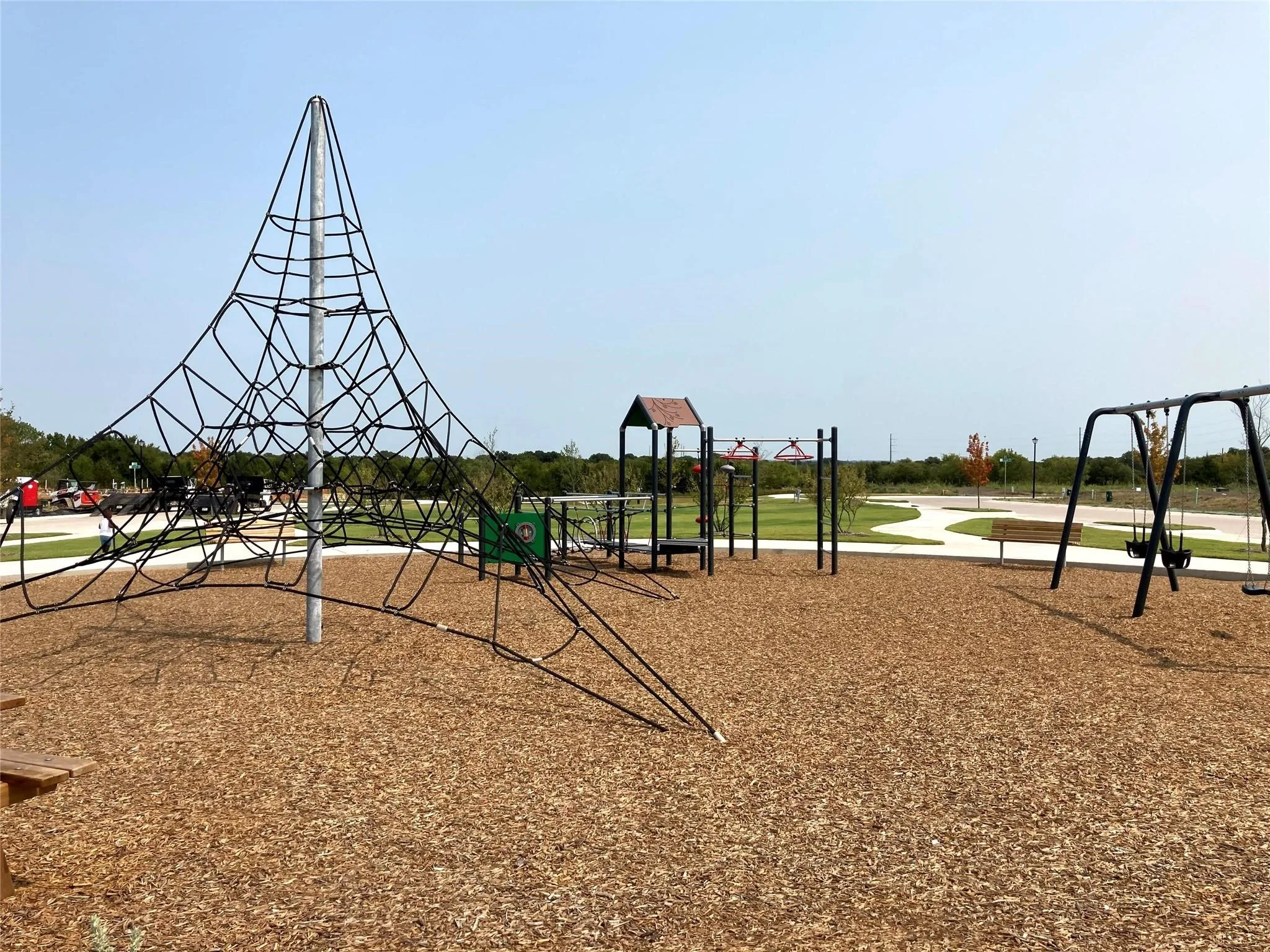Modern playground featuring a striking geometric climbing structure with rope elements, multi-level play tower with slide, and swing set