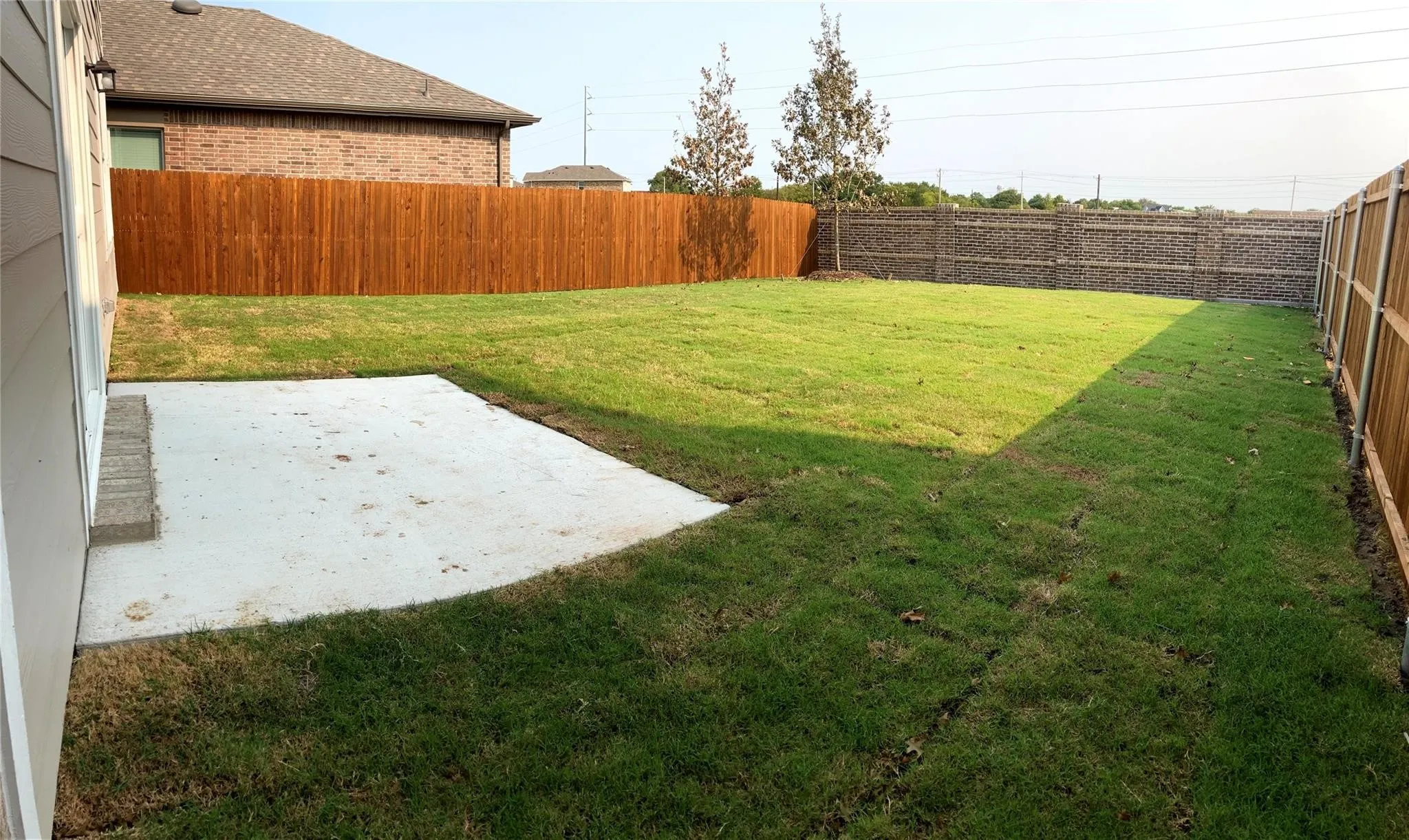 Expansive backyard featuring a concrete patio, a wooden privacy fence, and a brick-patterned fence
